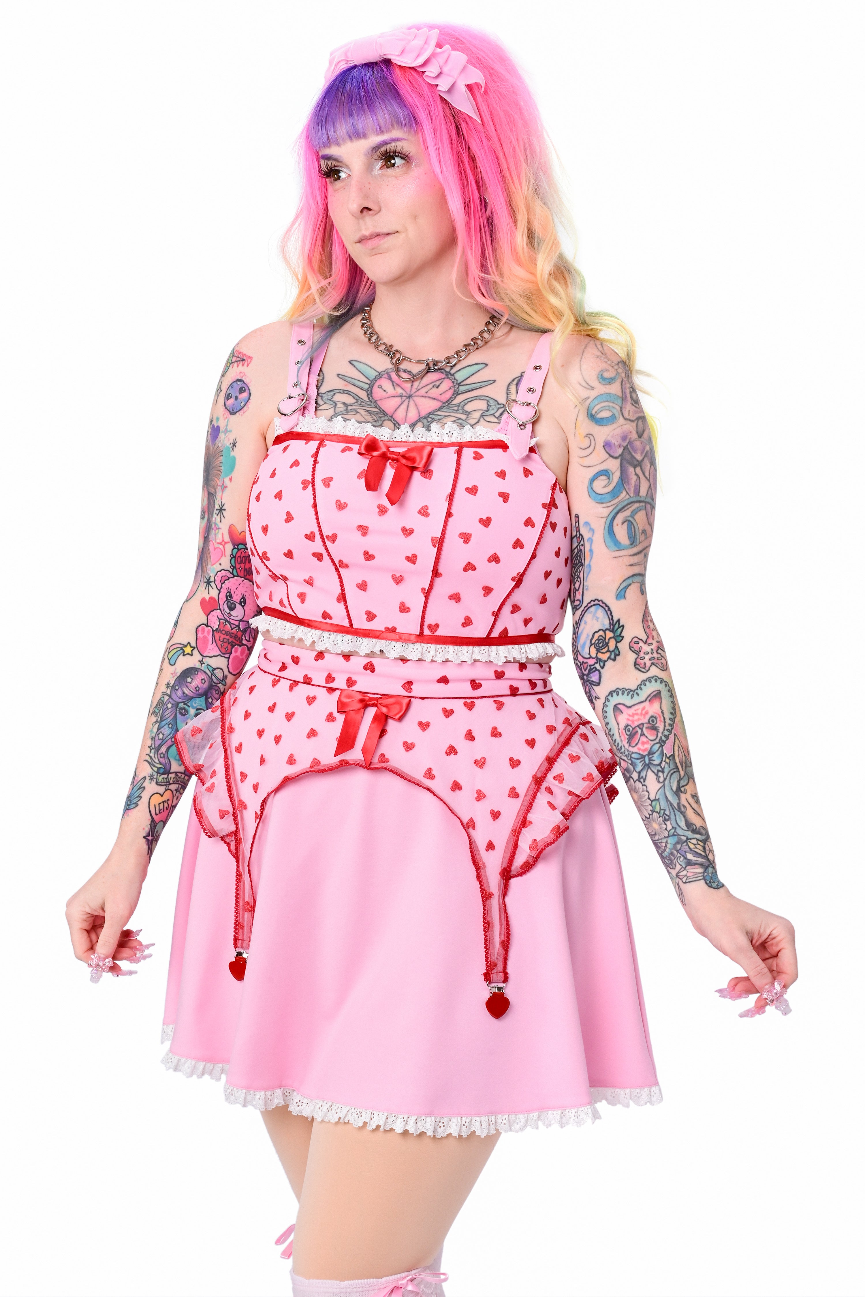 A person wearing a pink corset style crop top with a red mesh overlay, adorned with glittery hearts and a dainty pink bow at the neckline