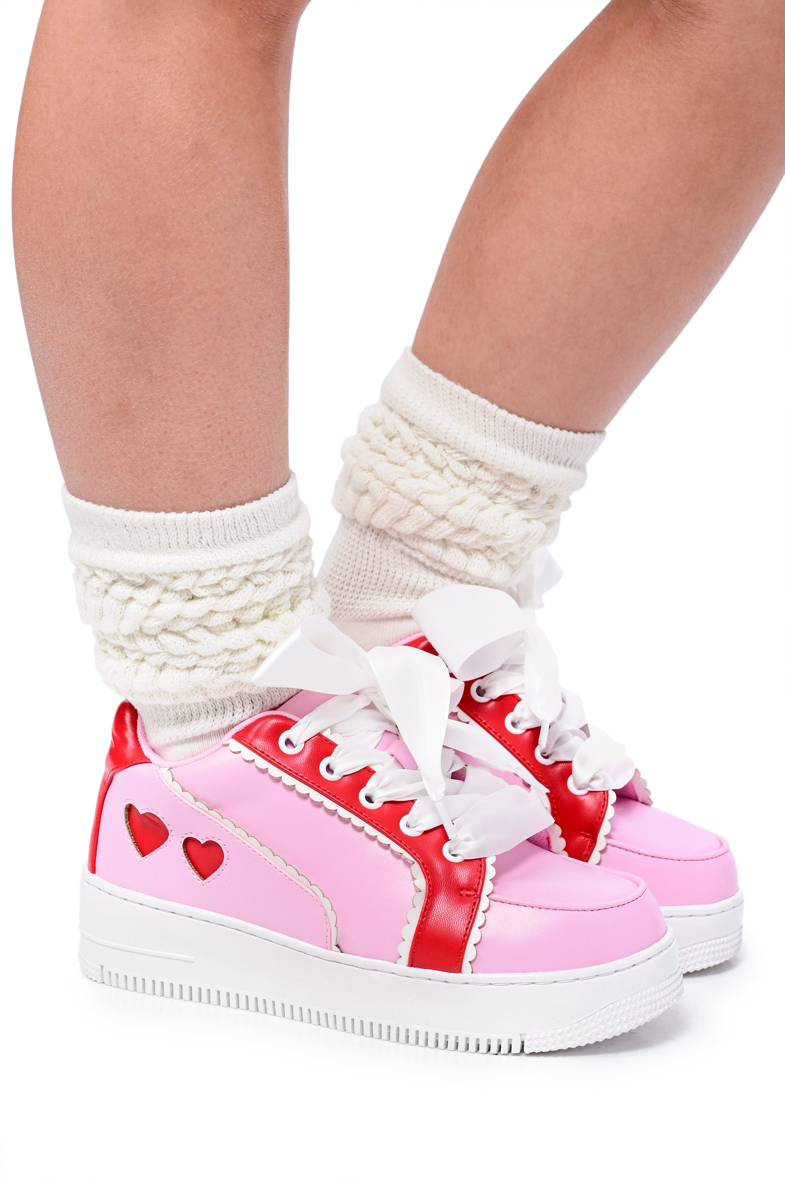 A pair of pink and red colorblock sneakers with heart cutouts on the sides and white socks. The sneakers have red heart accents and white laces.