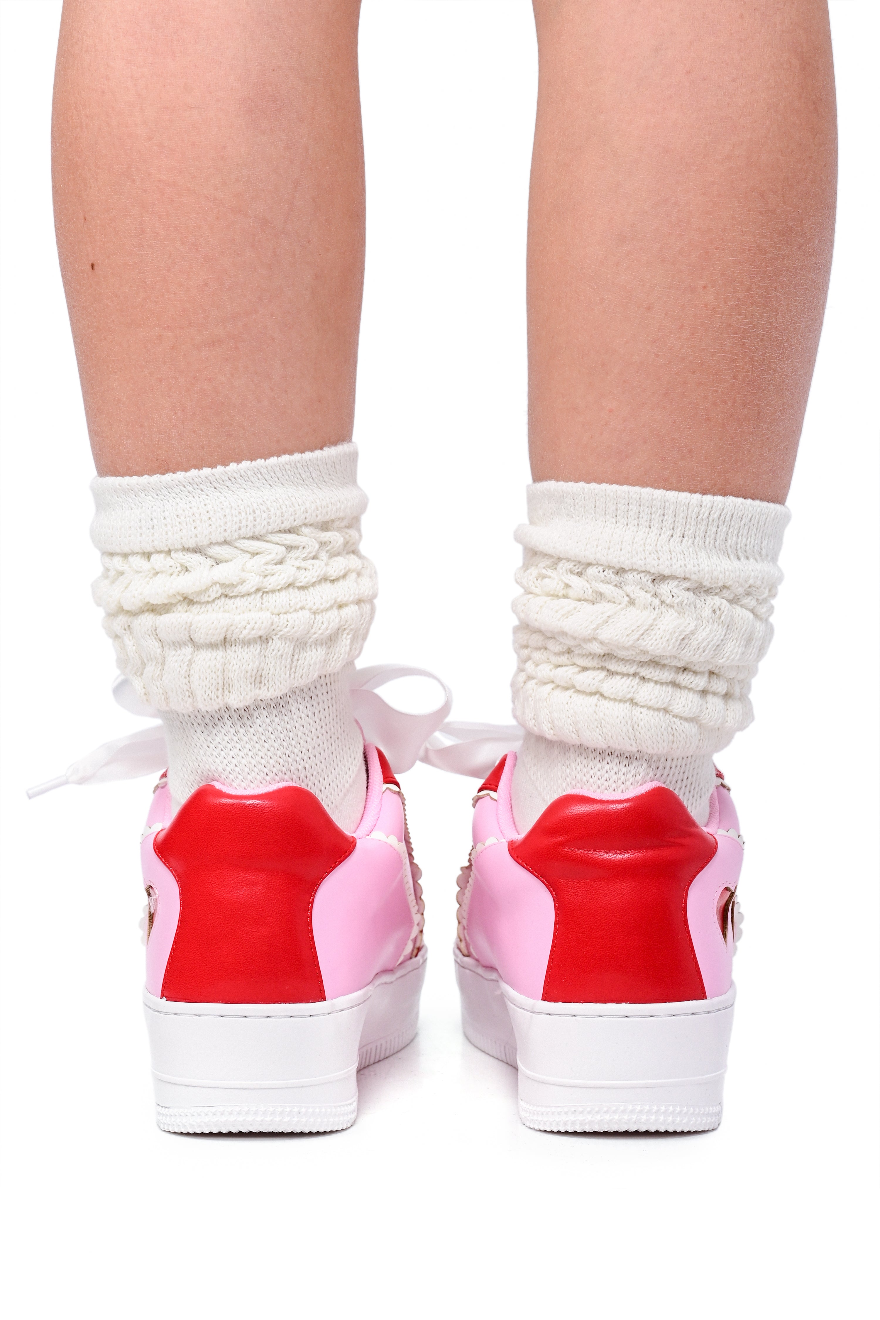 A pair of pink and red colorblock sneakers with heart cutouts on the sides and white socks. The sneakers have red heart accents and white laces.