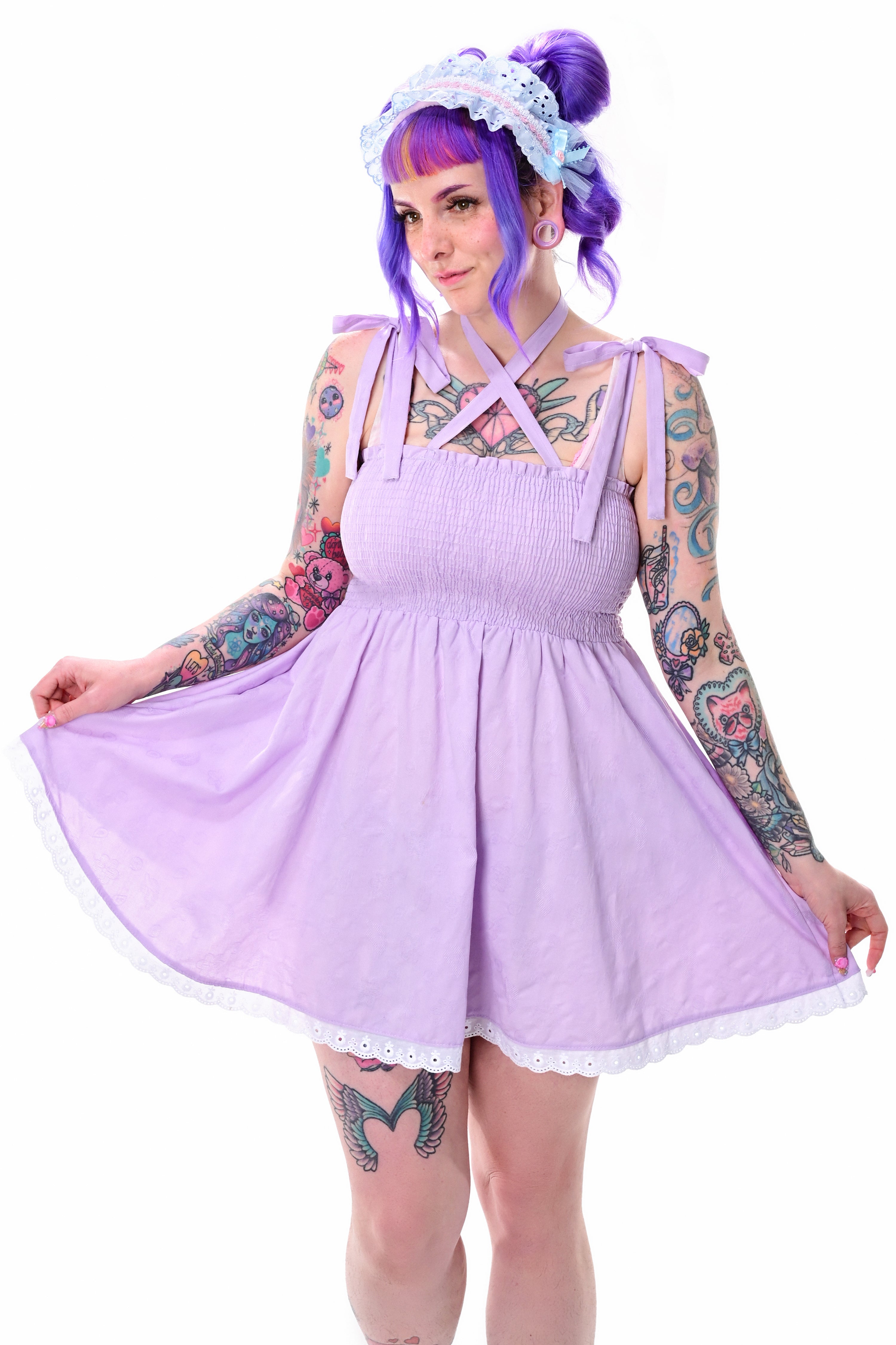 A moel wearing a lavender sundress with tie bow straps and a fully smocked bodice, standing against a white background.
