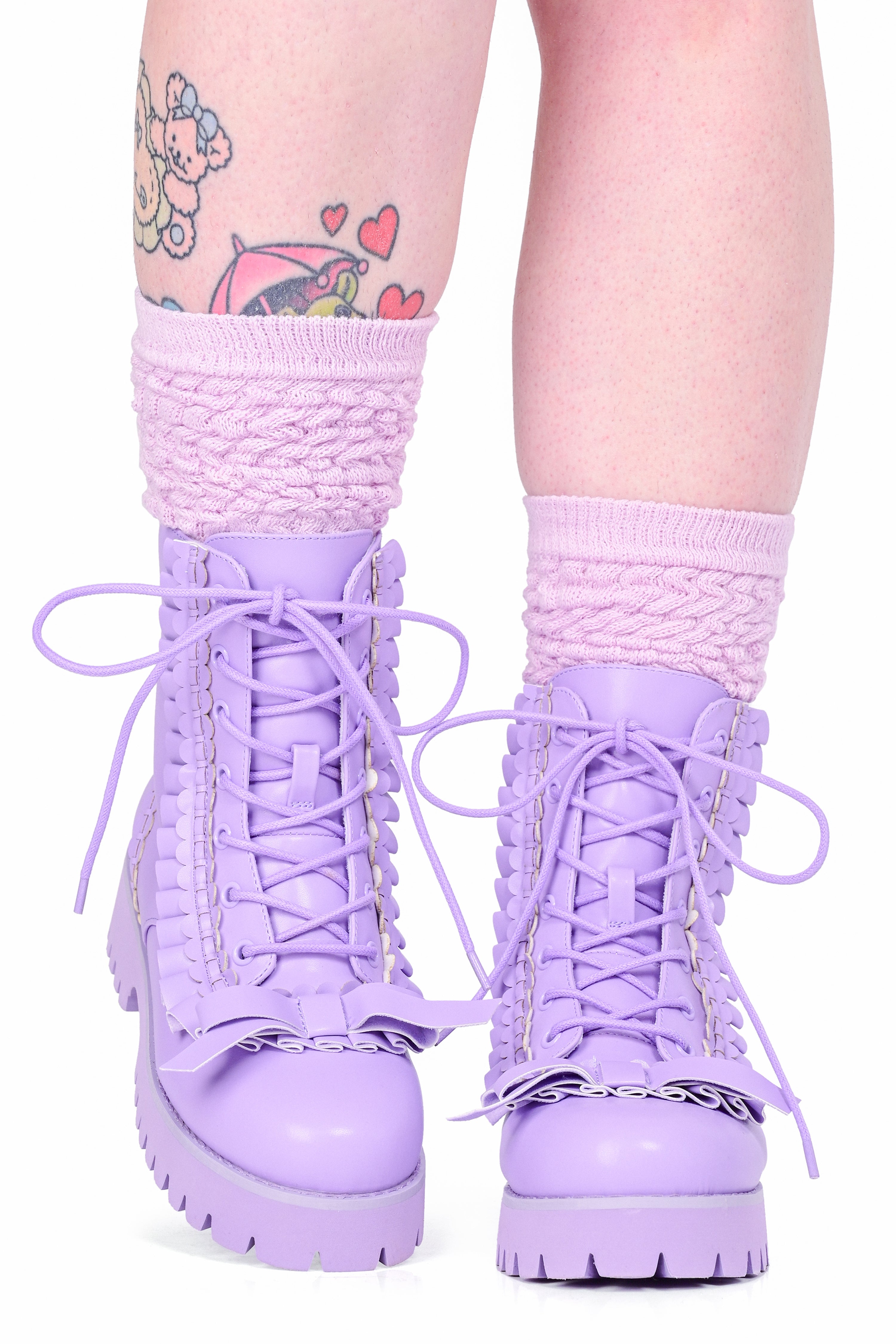 A model wearing a pair of lace up lavender boots with ruffle details and a bow