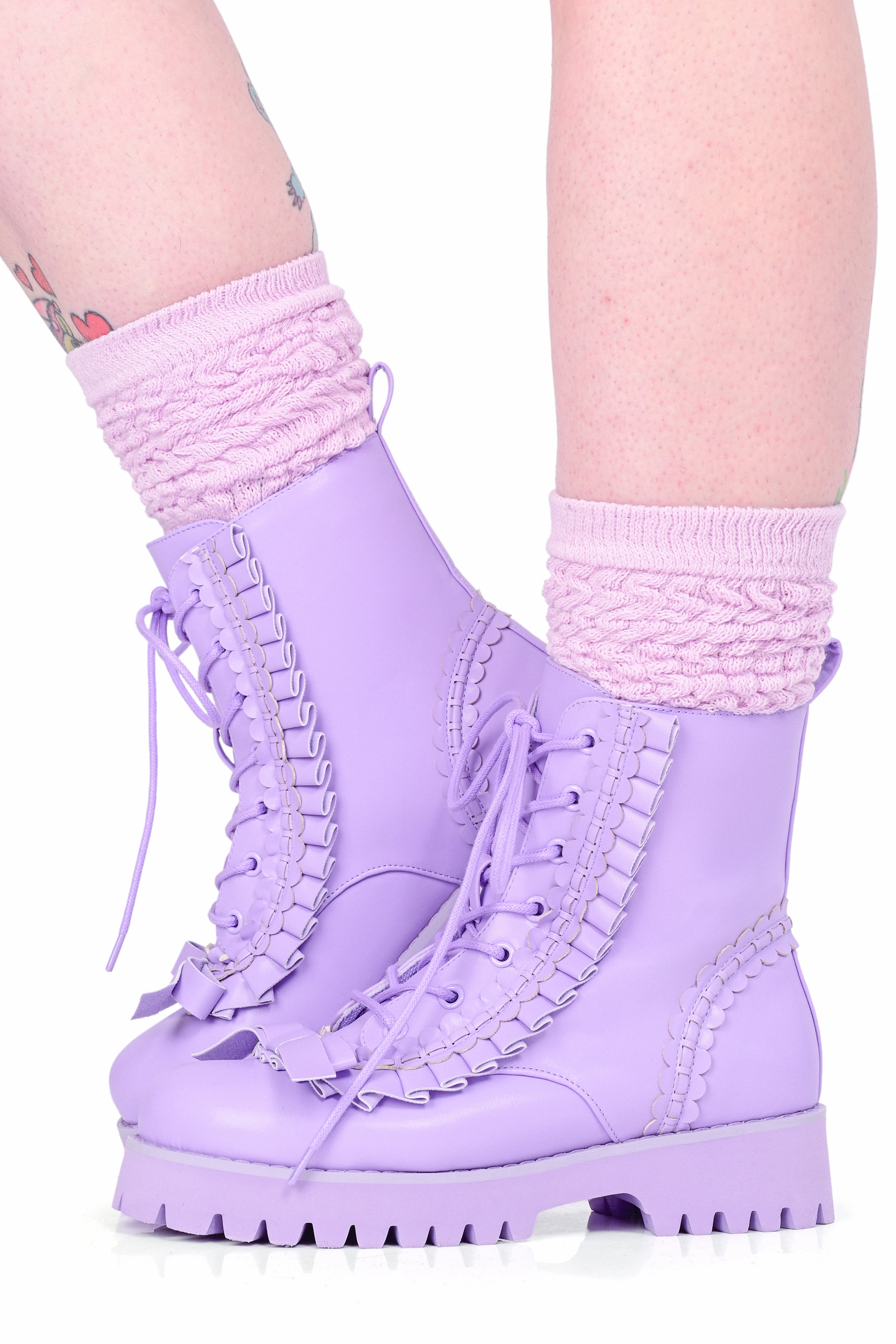 A model wearing a pair of lace up lavender boots with ruffle details and a bow