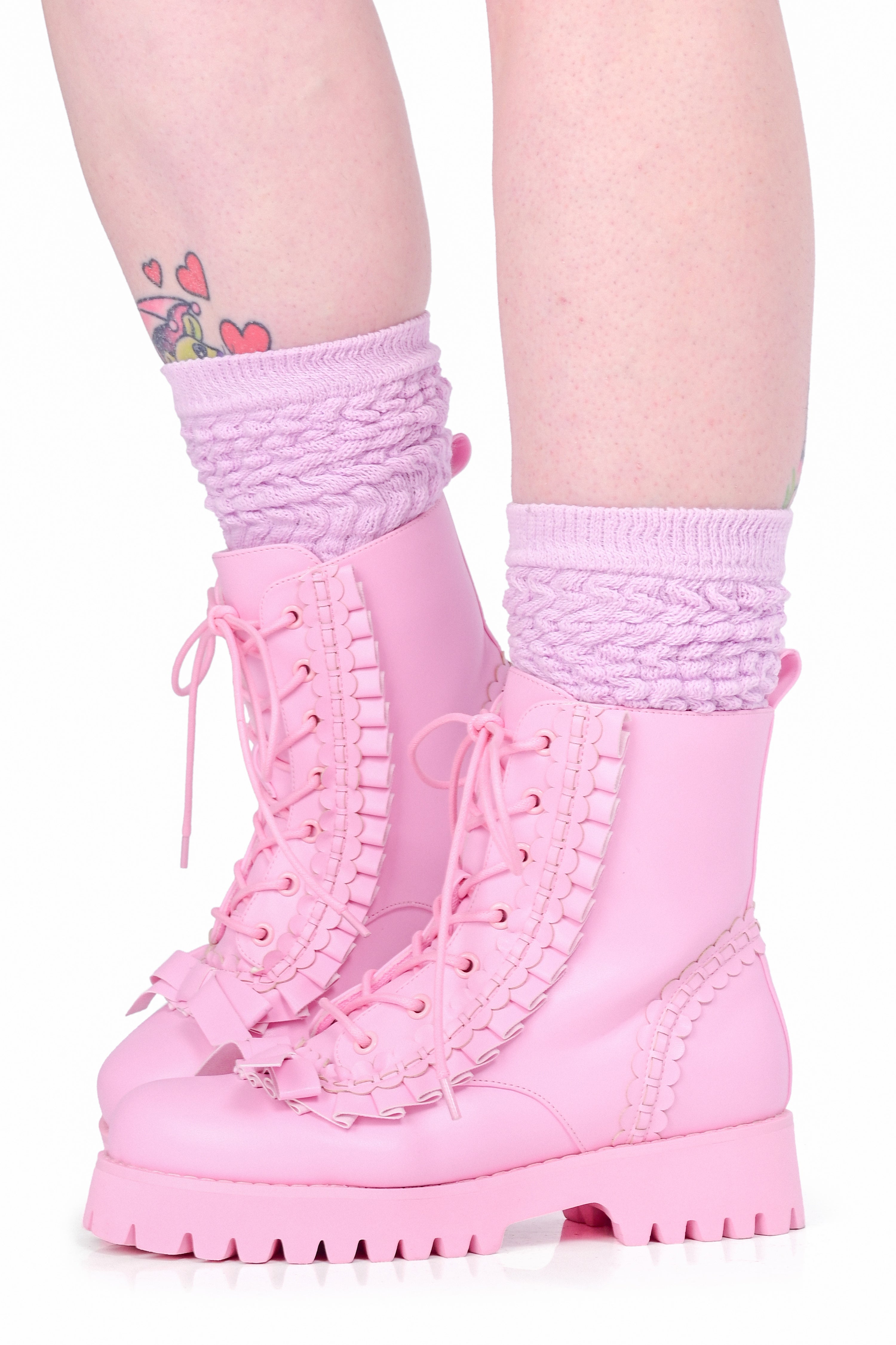 A model wearing a pair of lace up pink boots with ruffle details and a bow