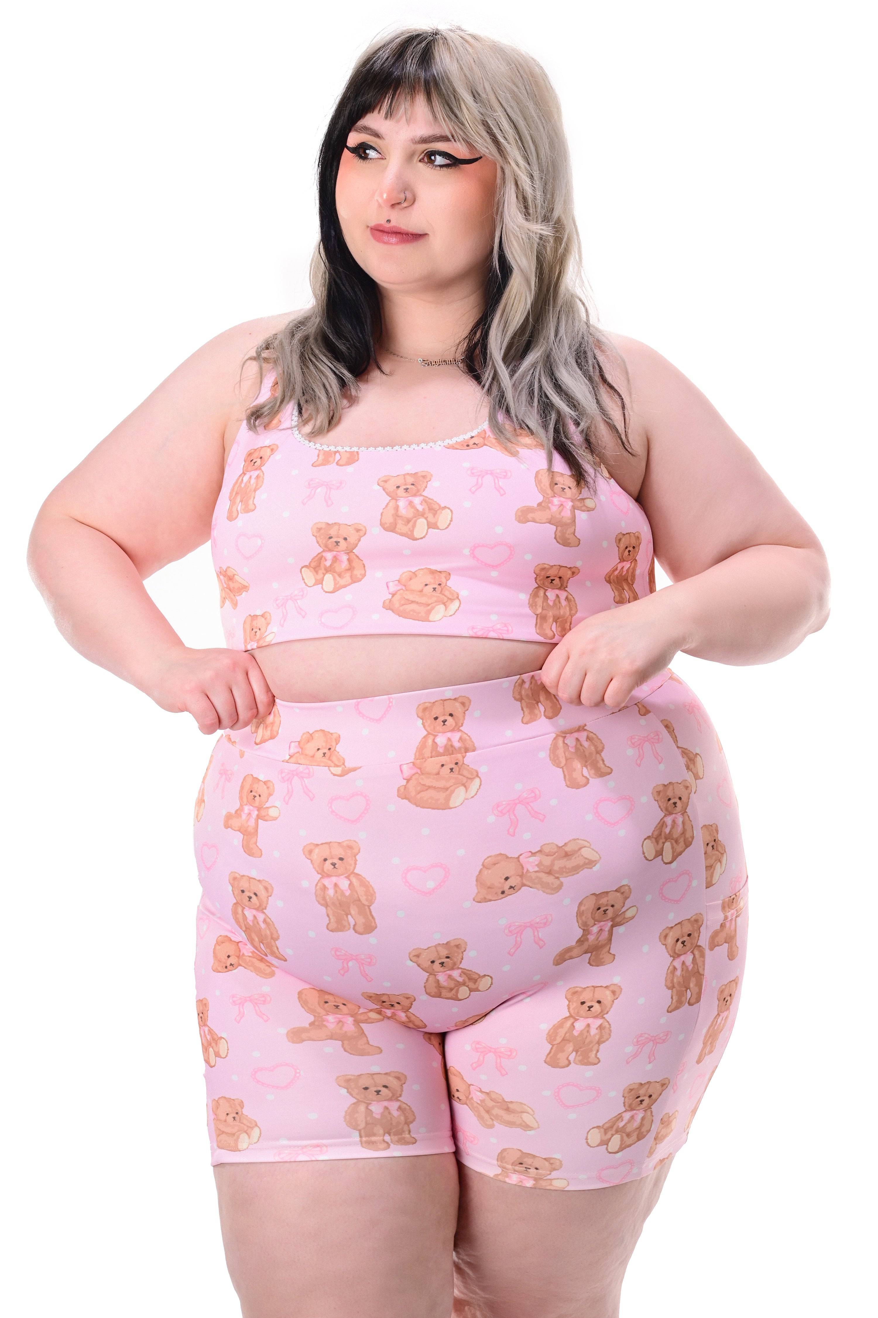 A model wearing a pink teddy bear print sports bra with delicate scallop lace trim, with a pair of matching biker shorts