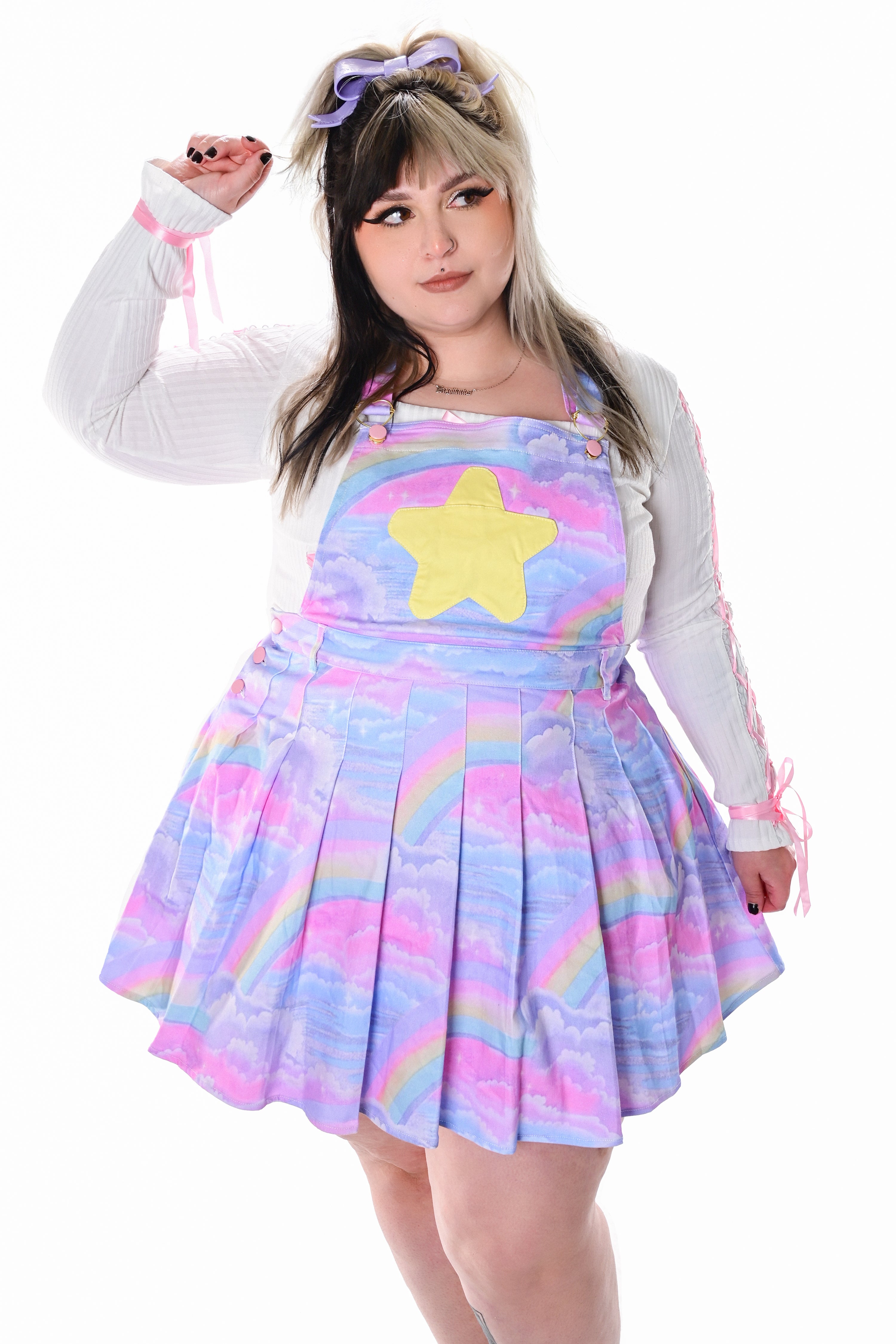 A model wearing a multicolored pinafore dress with a star applique, paired with a white long-sleeved top