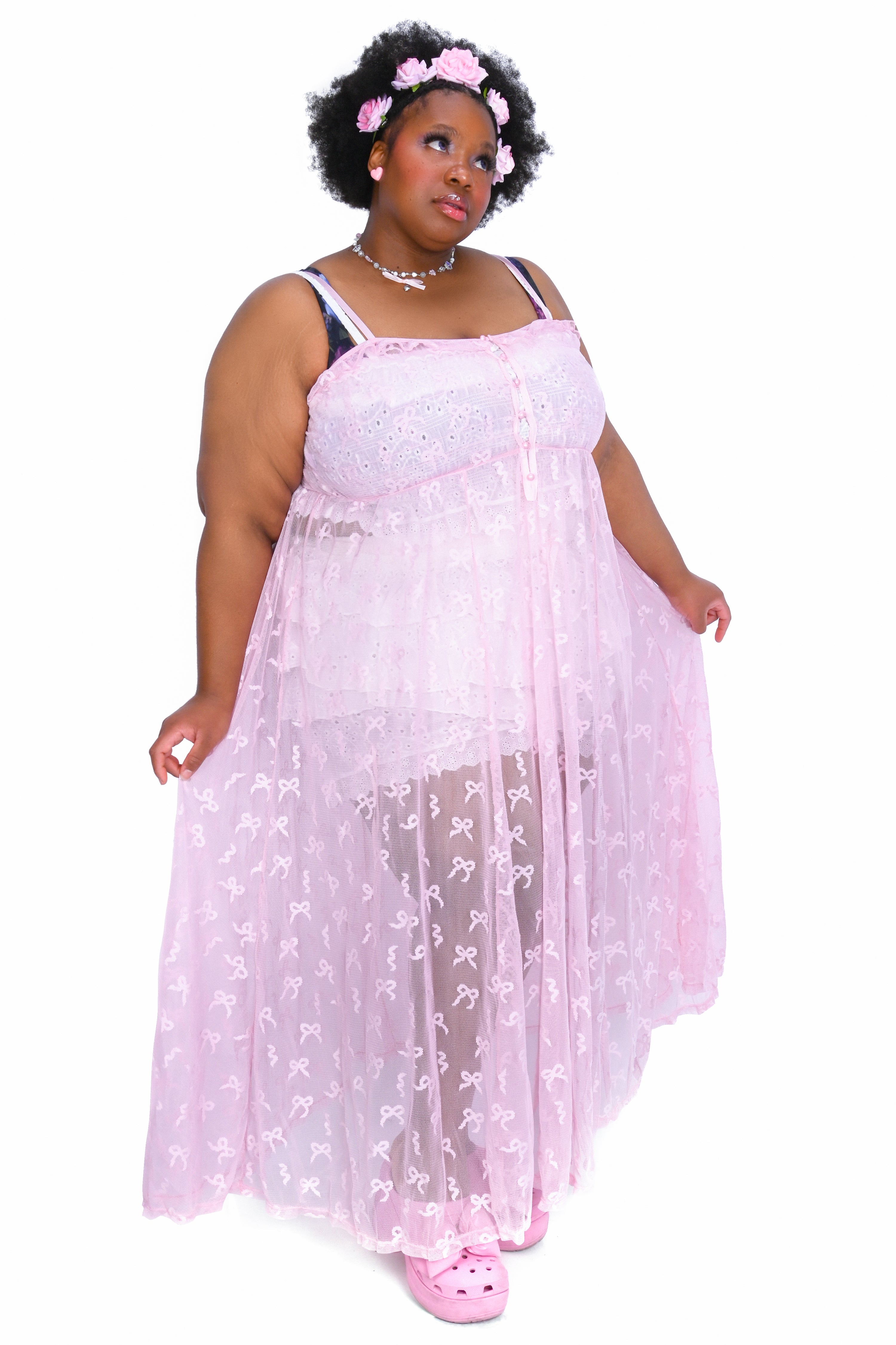 A person wearing a sheer pink maxi dress with adjustable straps and a front button closure.
