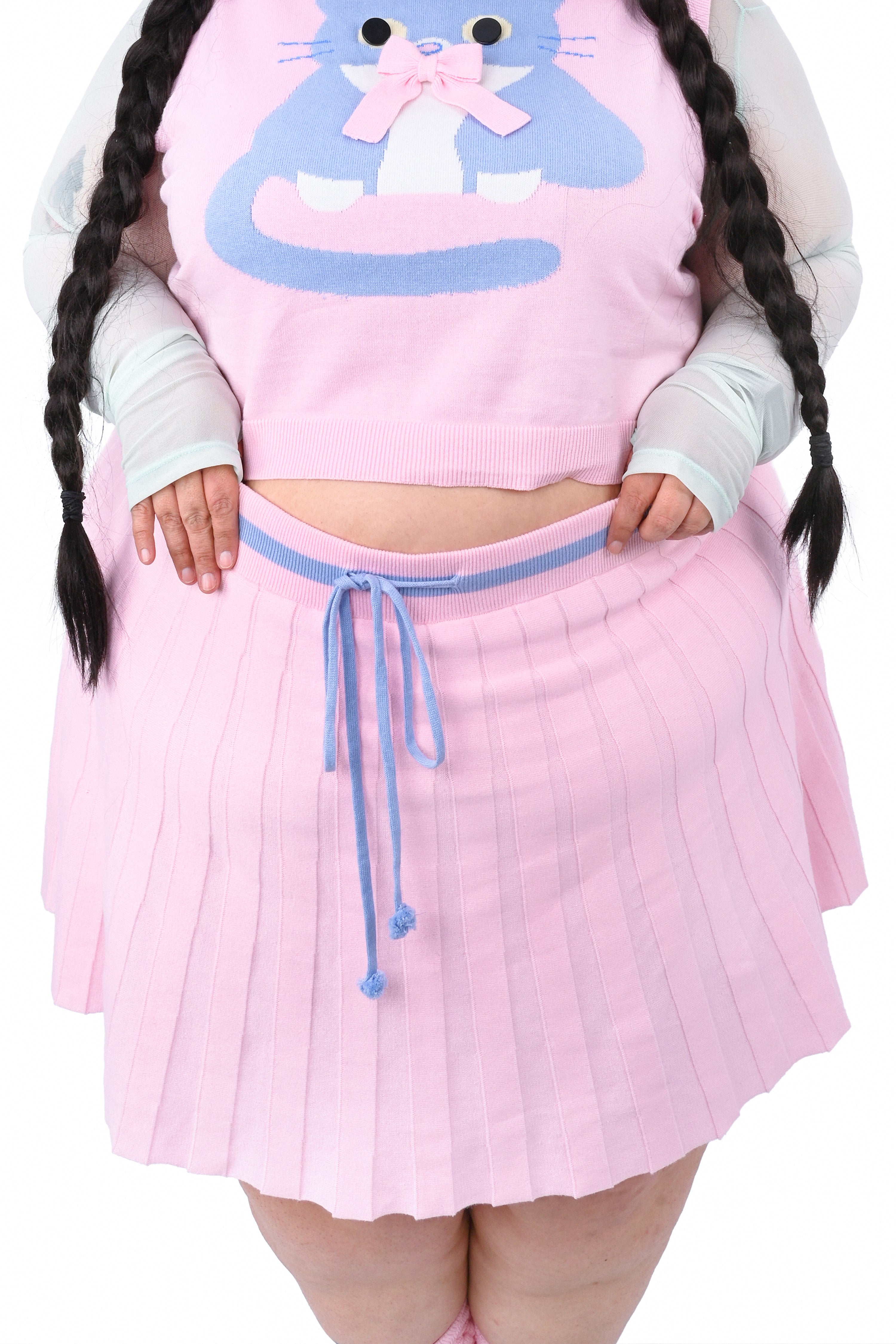 A person wearing a pink knit pleated skort and a matching sweater vest with a cat graphic