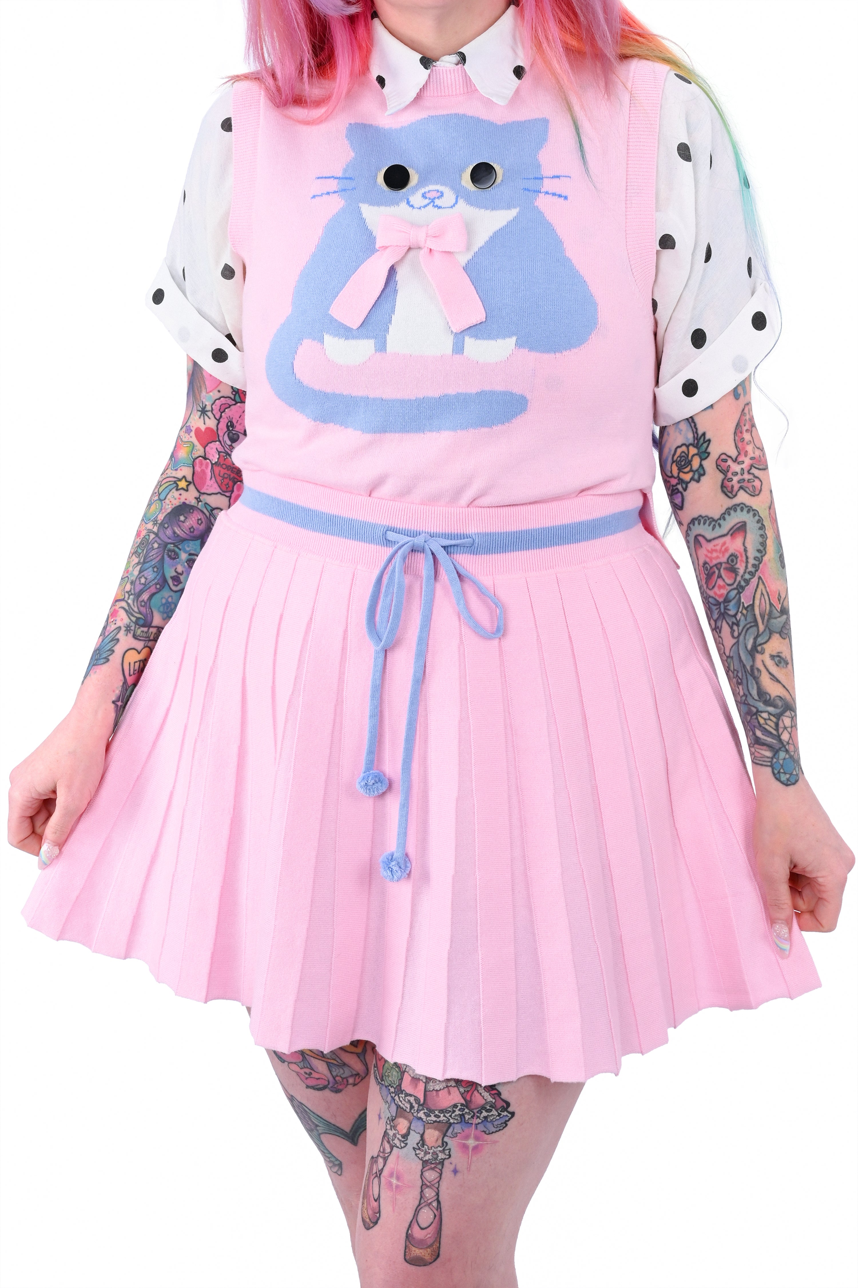 A person wearing a pink knit pleated skort and a matching sweater vest with a cat graphic