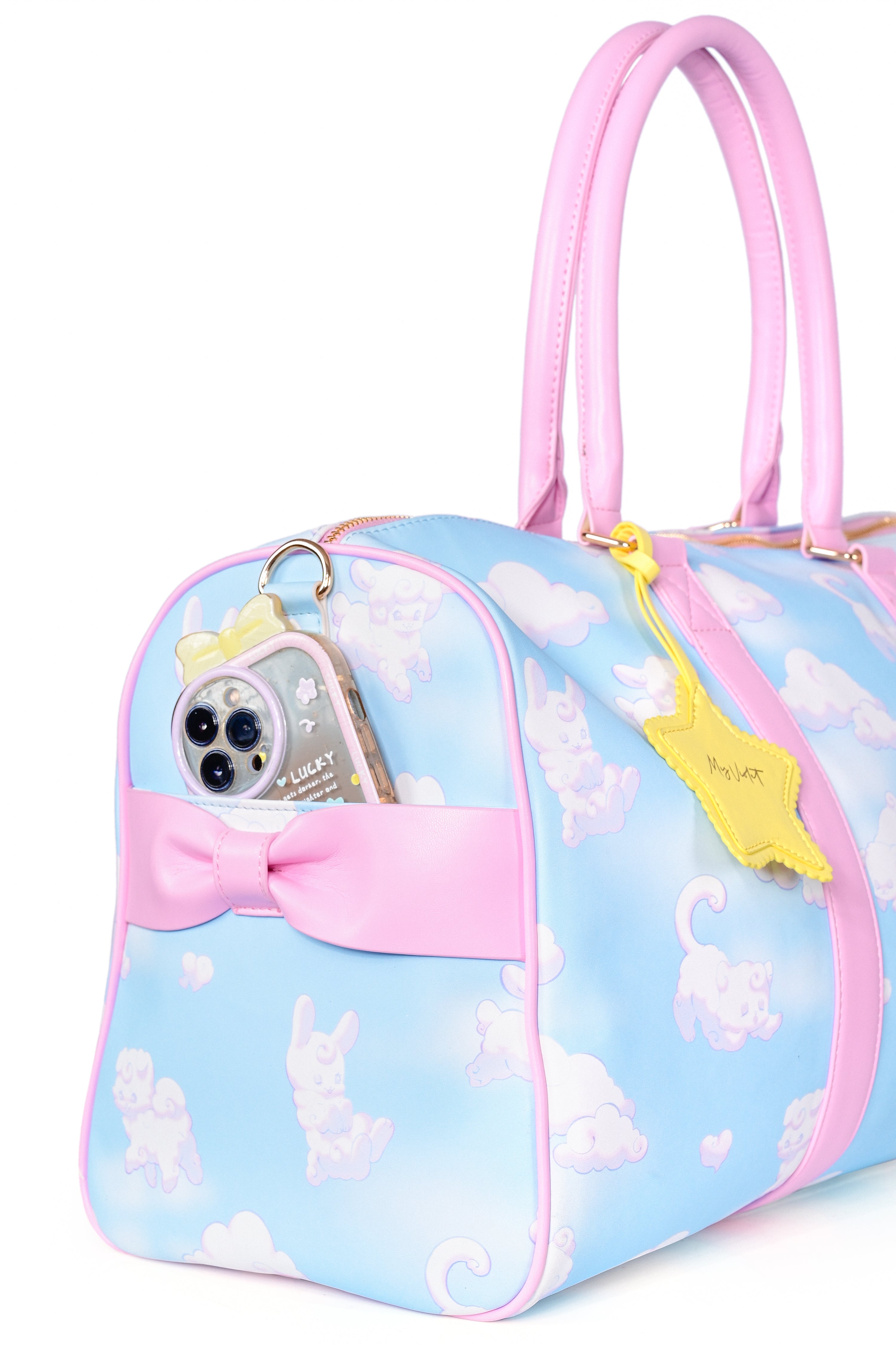 A weekender bag with a blue and white cloud pattern, featuring pink trim, two handles, and a detachable shoulder strap. It includes a yellow star-shaped charm attached to one of the handles.