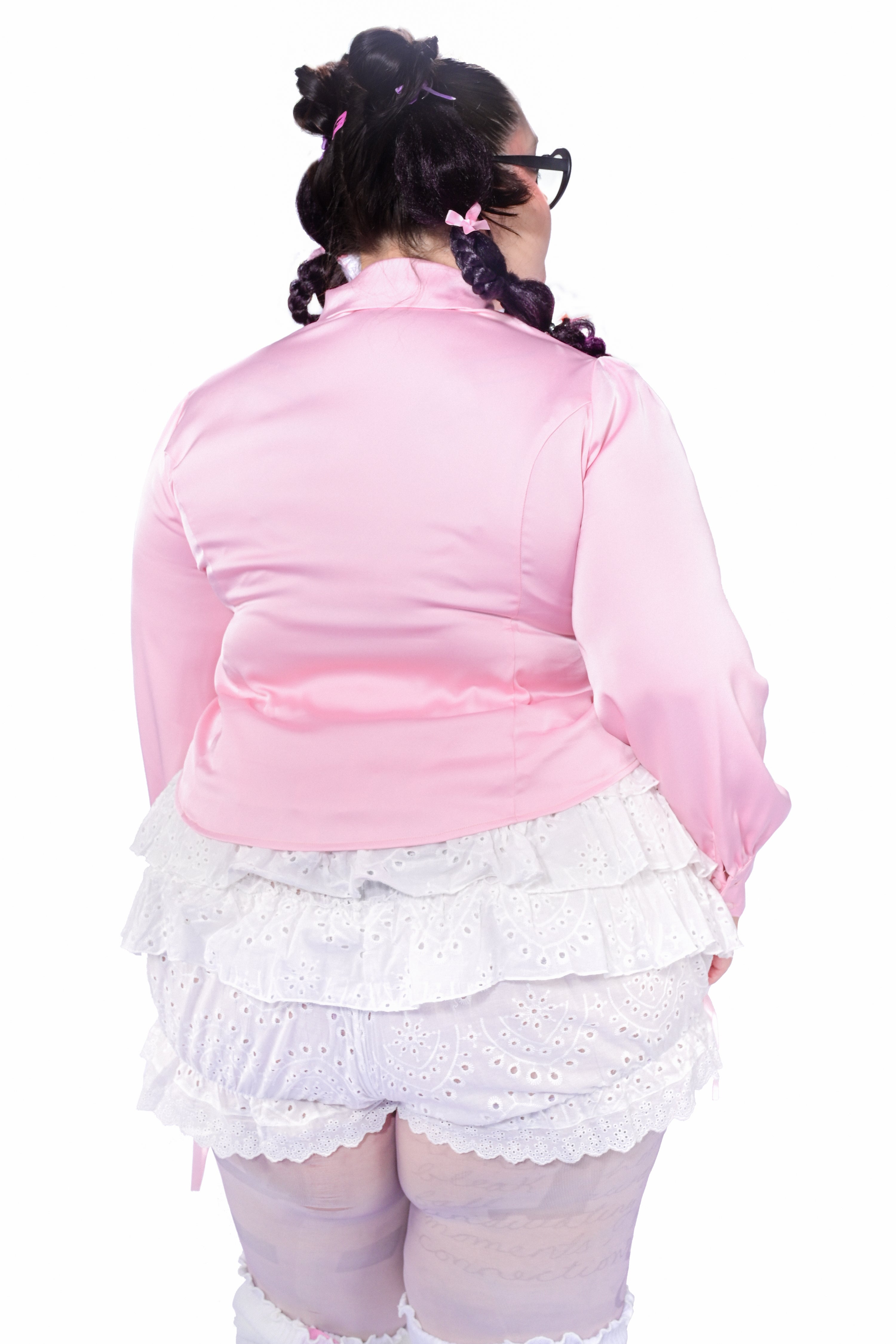 A model wearing a pink button-up blouse with a heart cutout at the chest, paired with white lace shorts.