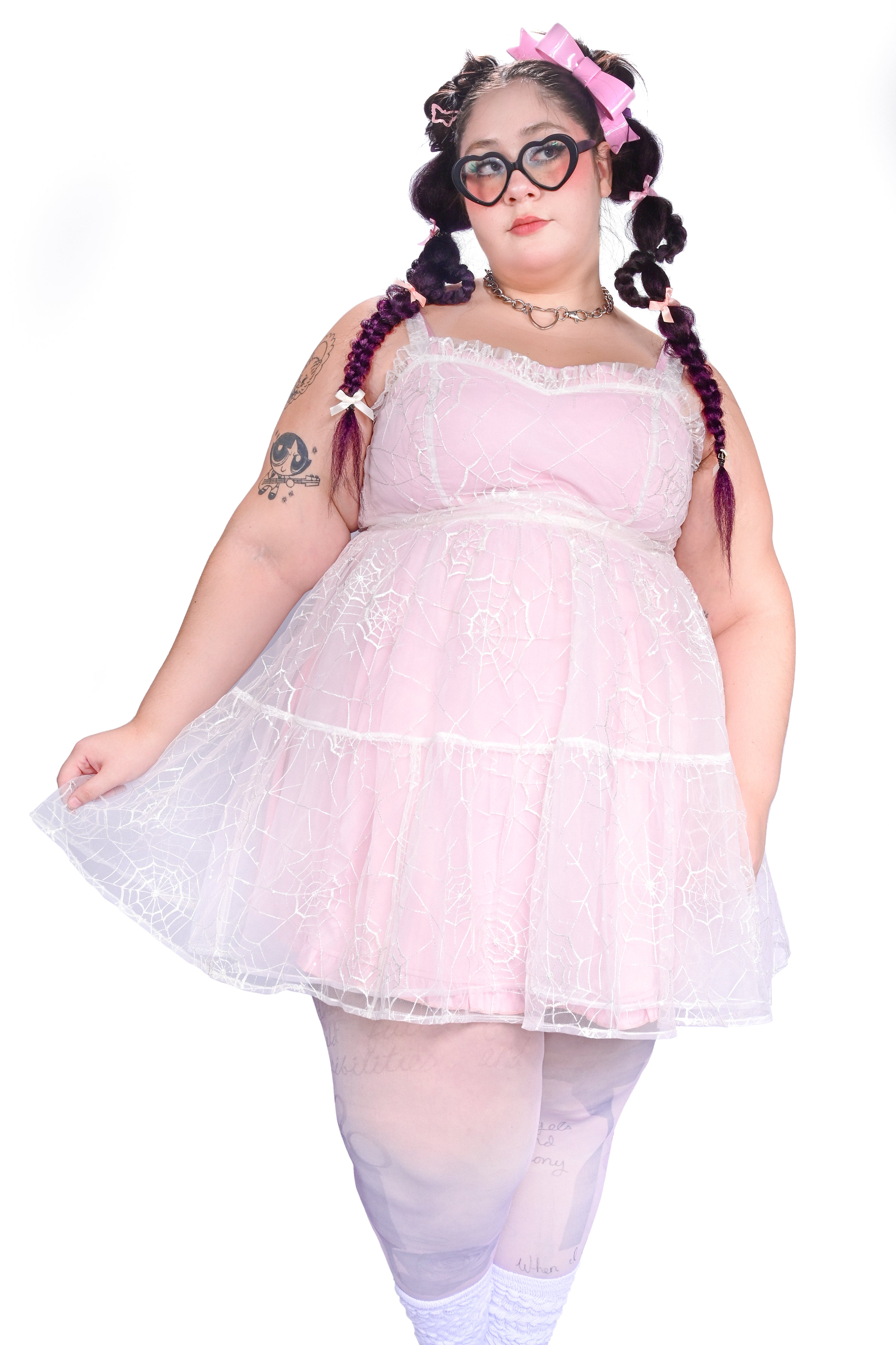 A person wearing a sheer mesh overdress with embroidered cobwebs and sequin dew drops, paired with a pink inner dress.