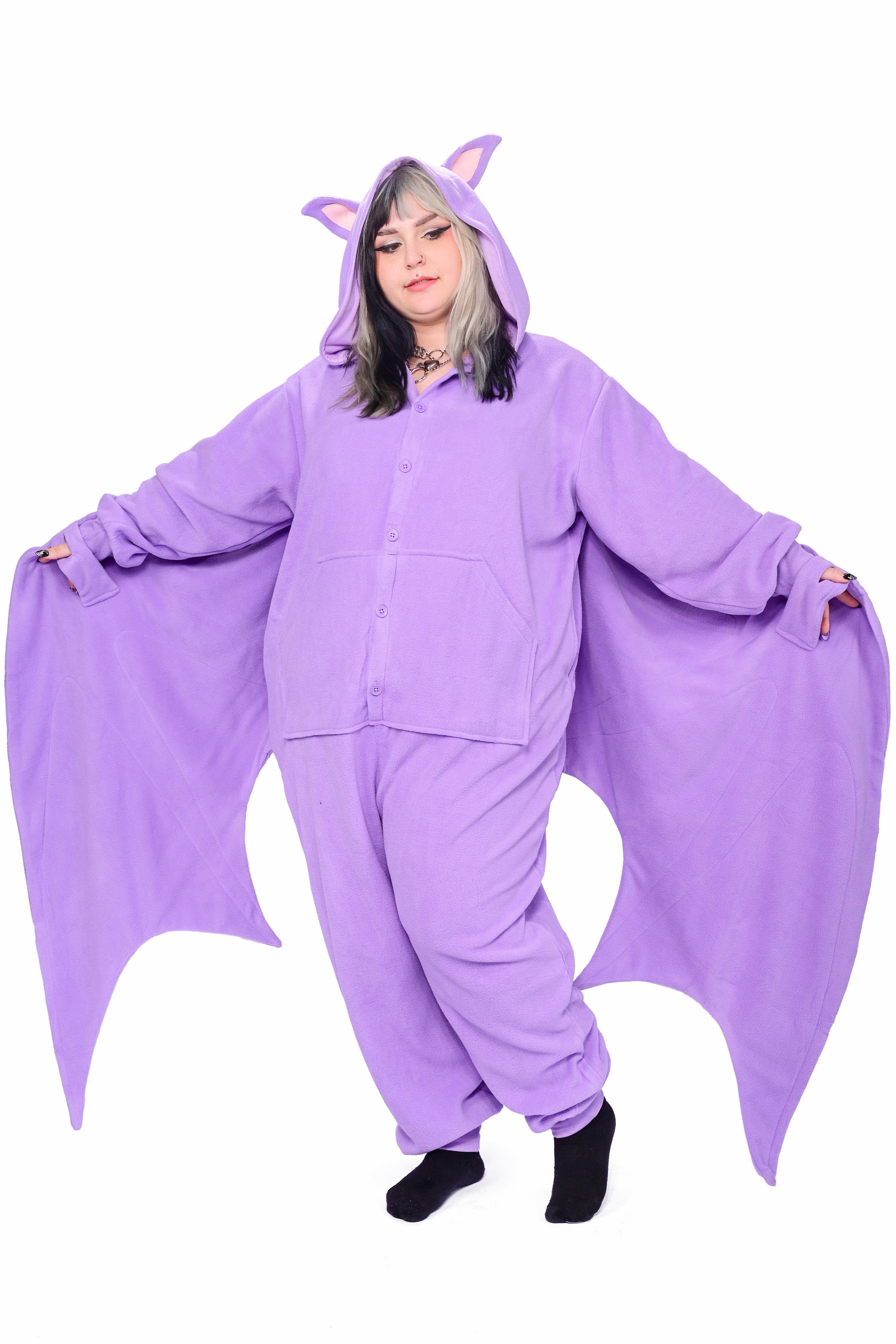 A person wearing a purple fruit bat onesie with a hood featuring bat ears, with both wings extended
