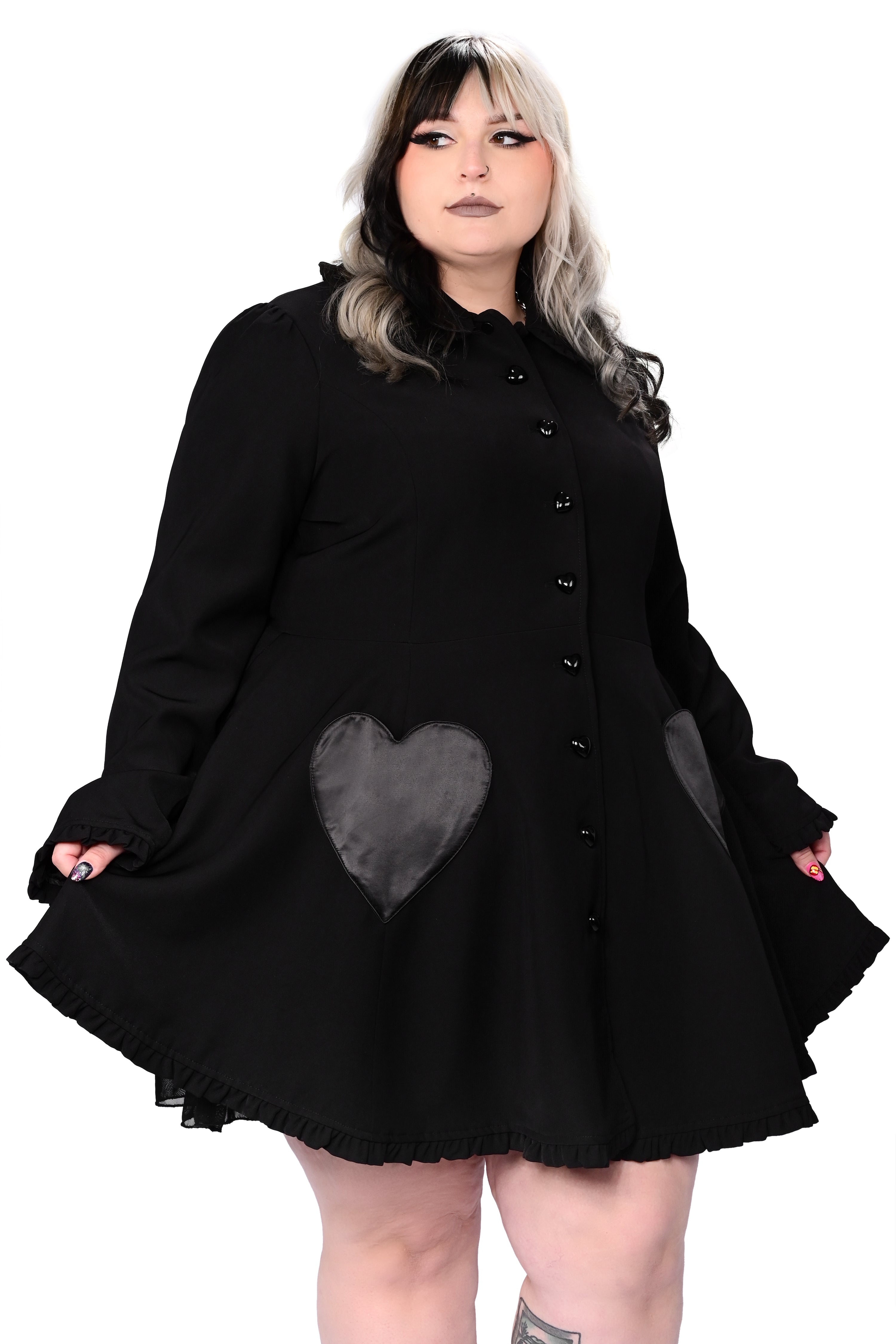 A person modeling a black coat with detachable cat ears and frilly details at the collar and hem. The coat features heart-shaped pockets and buttons, and is fitted at the bodice.