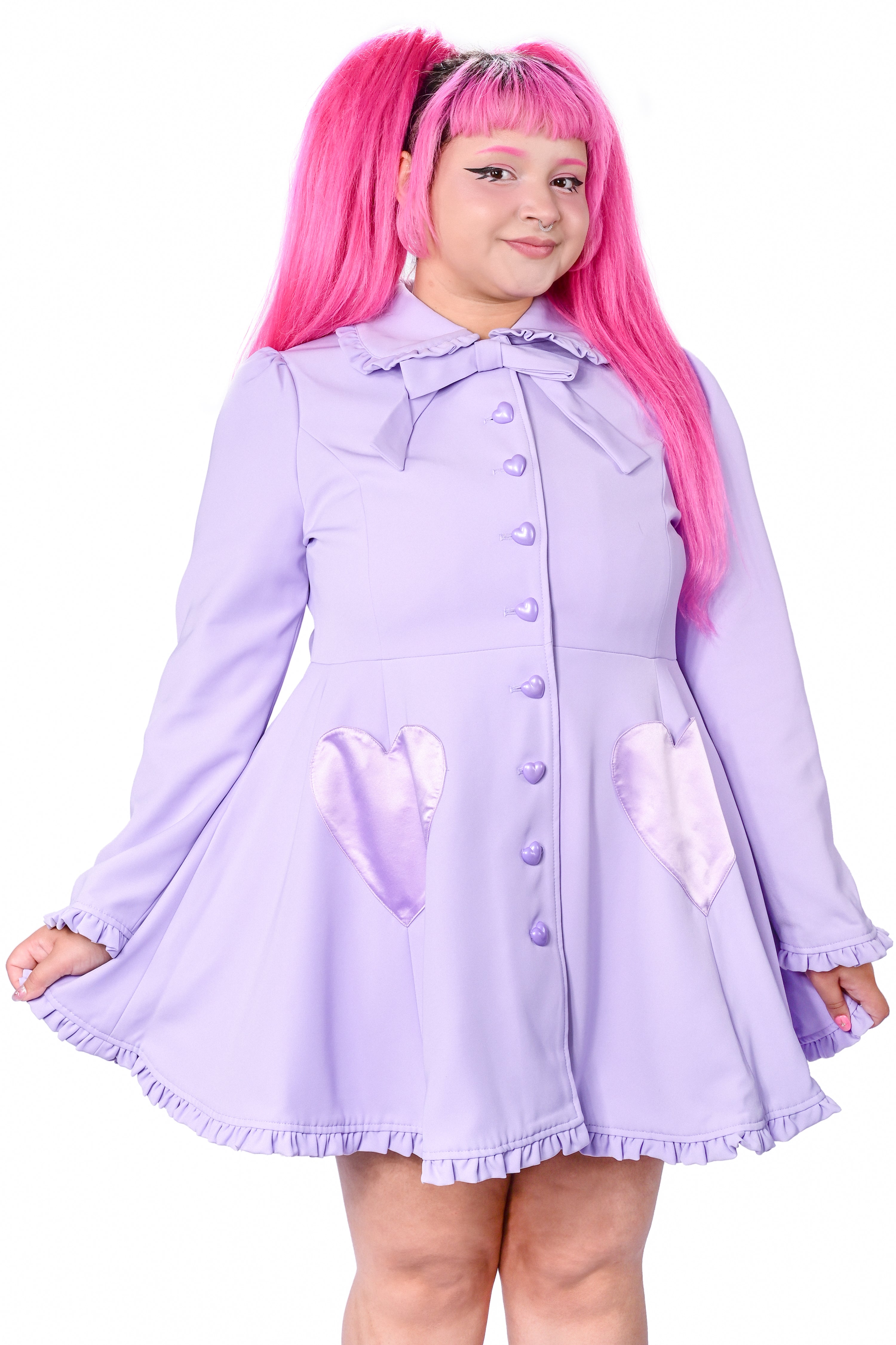 A person modeling a lavender coat with detachable bunny ears and frilly details at the collar and hem. The coat features heart-shaped pockets and buttons, and is fitted at the bodice.