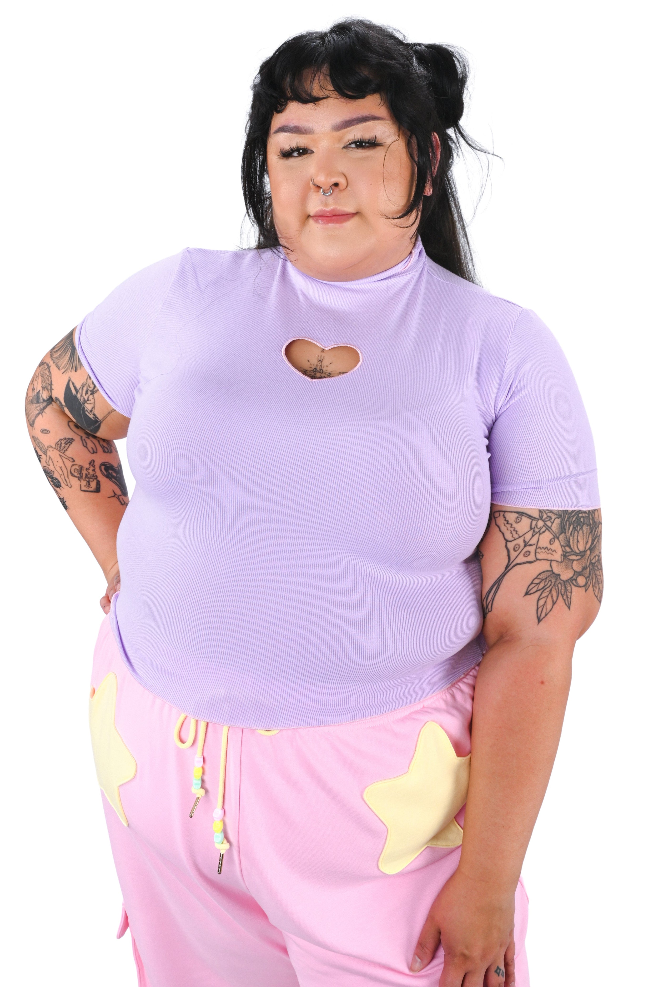 Person wearing a light purple t-shirt with a heart design and pink pants with yellow accents on a white background