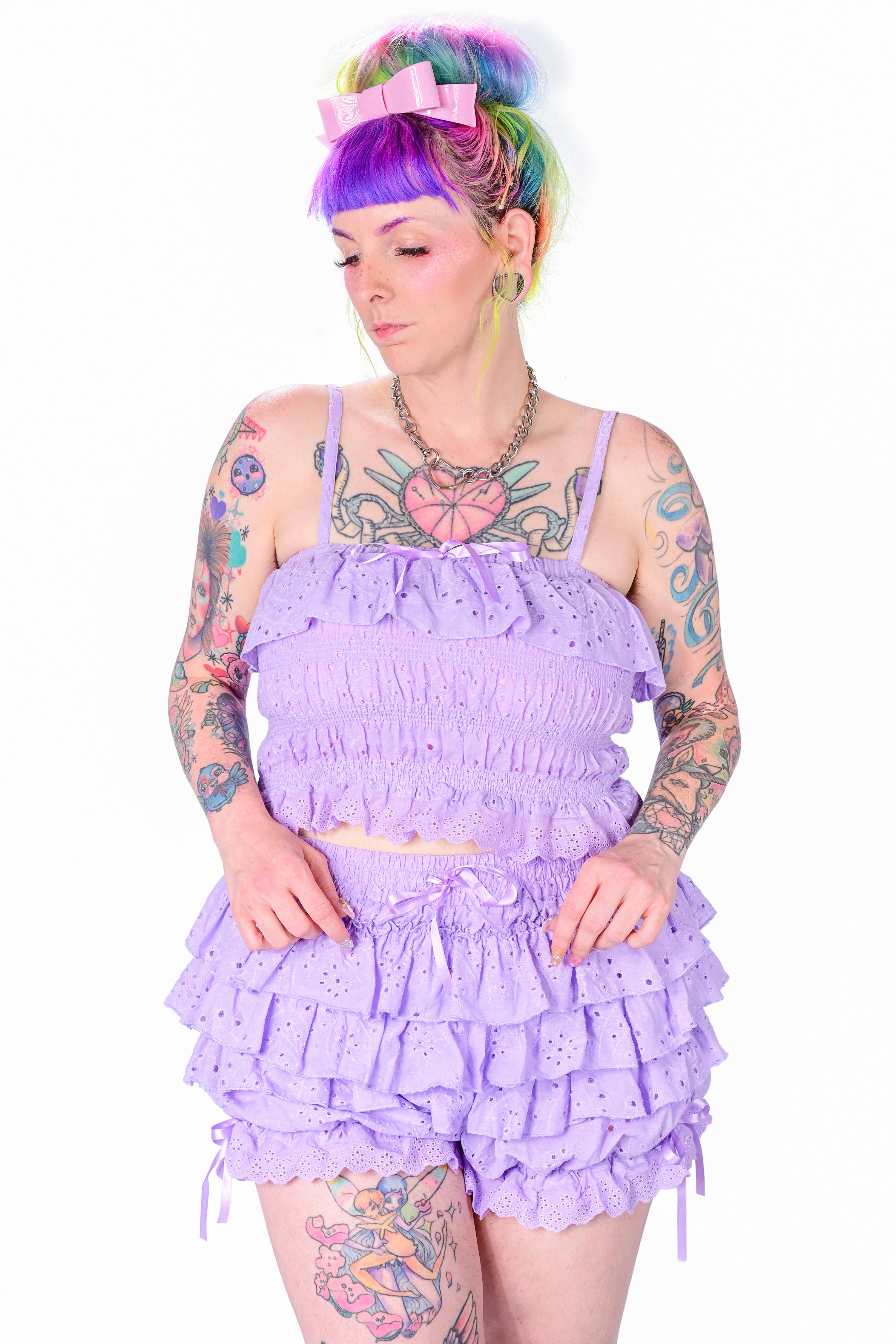 A person wearing a purple, ruffled, eyelet lace camisole top with adjustable straps and satin bows, paired with matching shorts.