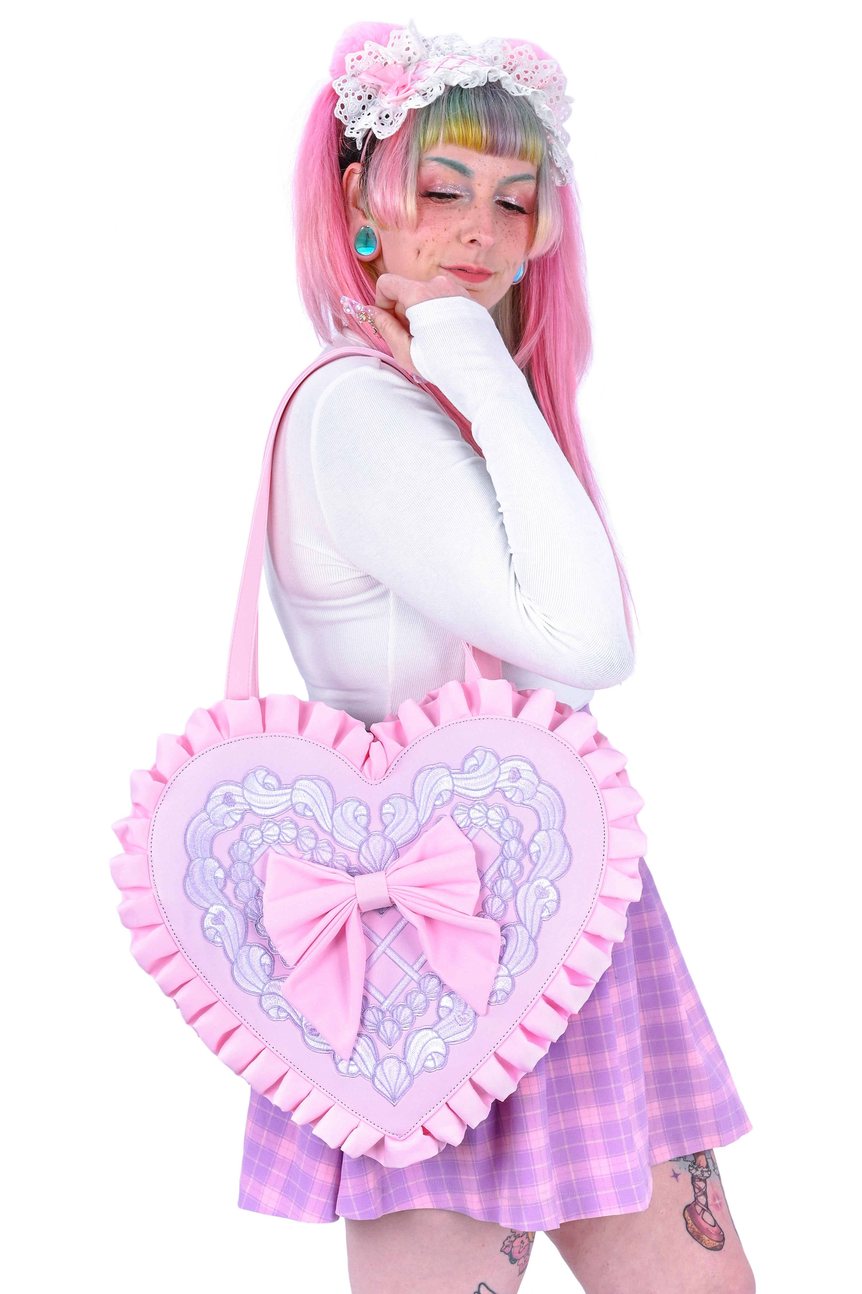 Person holding a pink heart-shaped bag with embroidery details on a white background