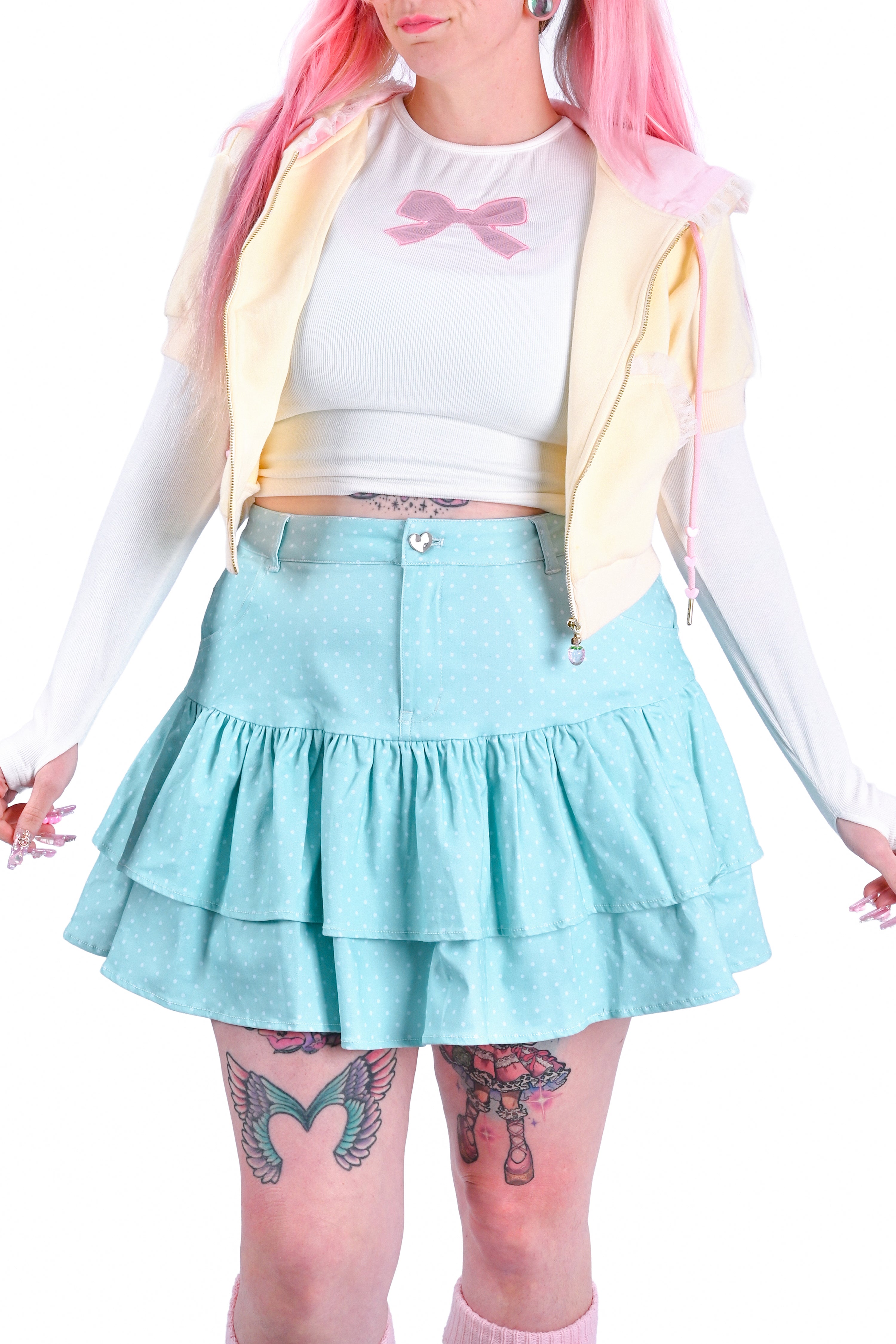 Person wearing a colorful outfit with a mint polka dot skirt, white top, and yellow jacket.