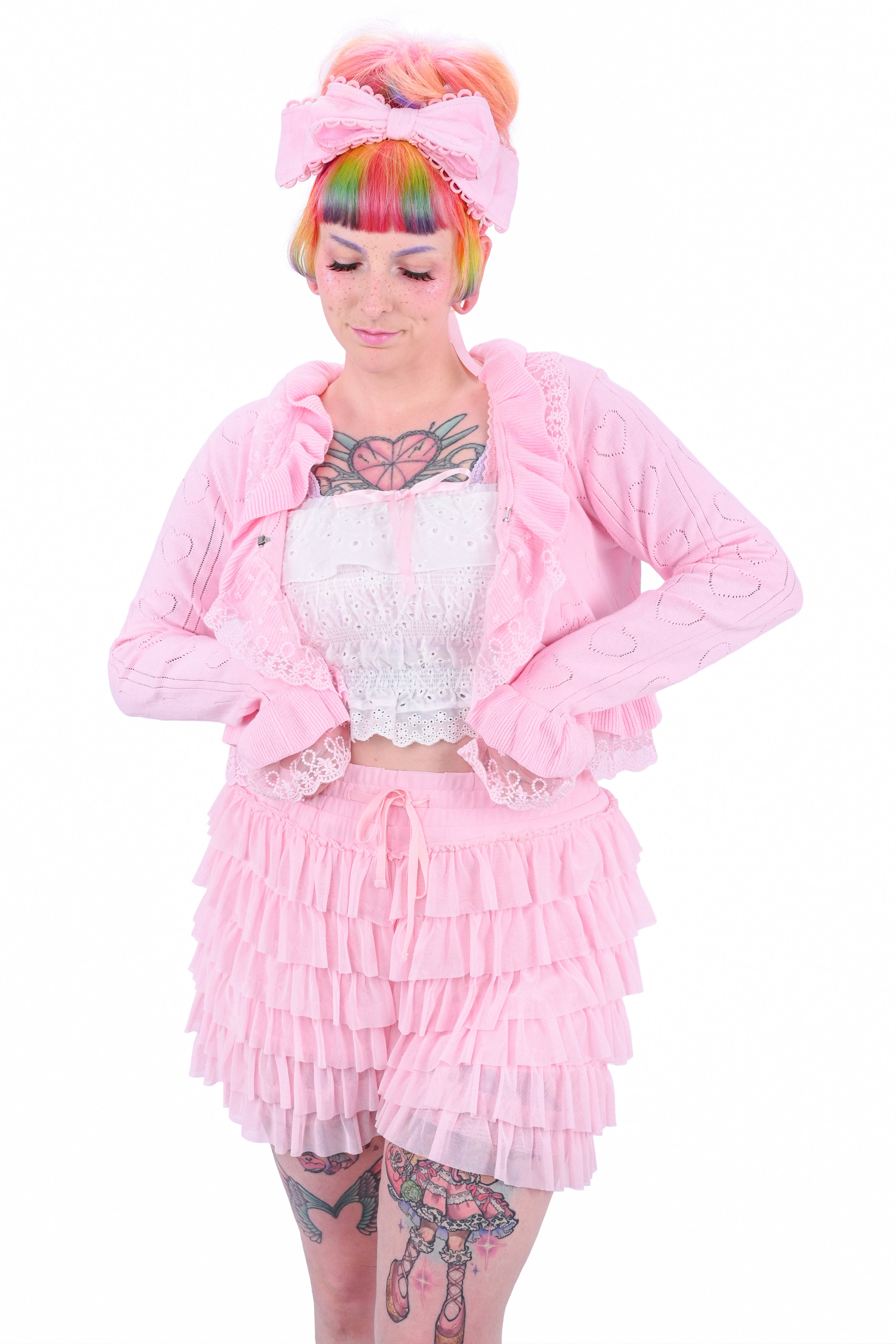 A person wearing pink ruffled mesh shortes and a matching white camisole and pink cardigan