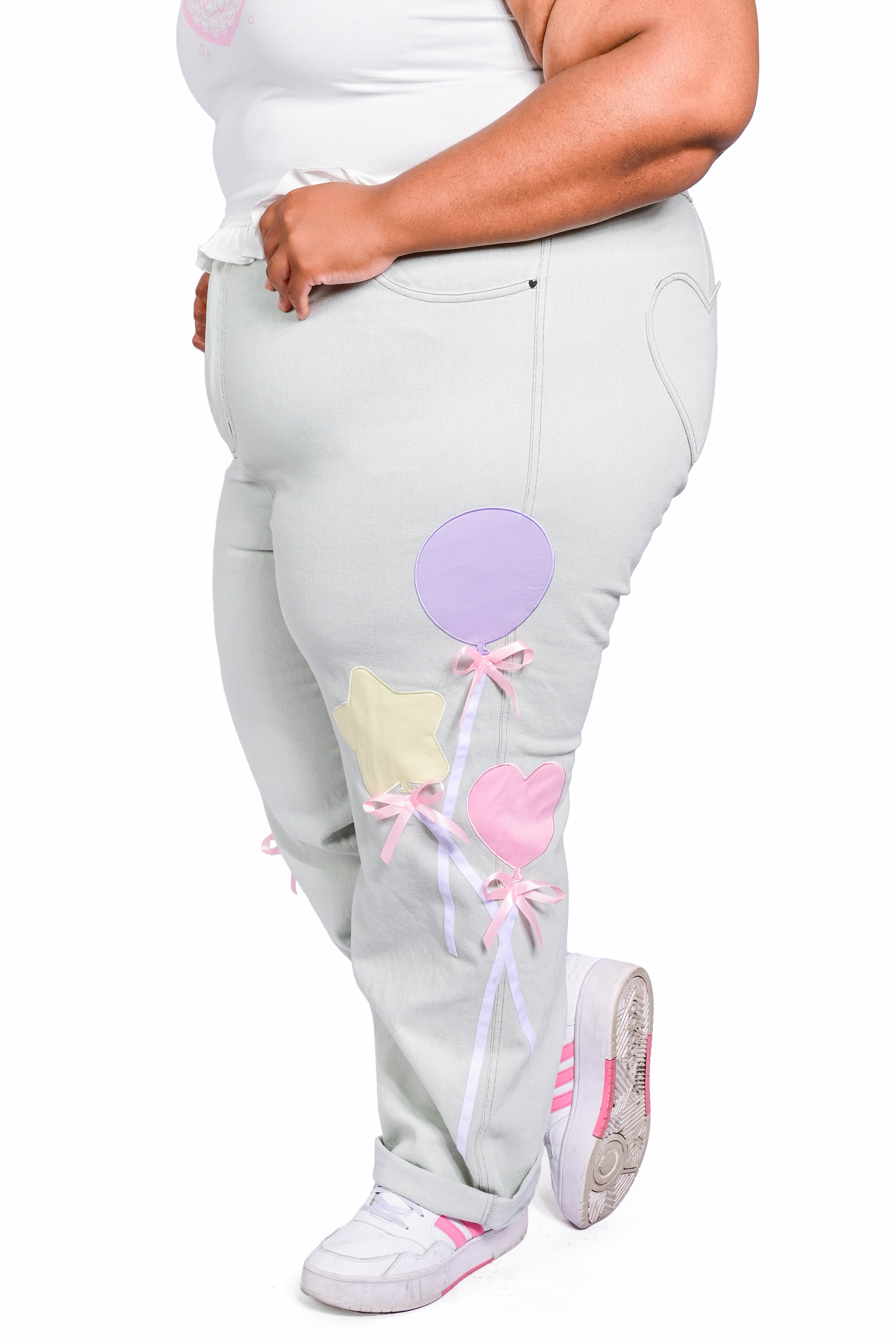 A model wearing a pair of light wash denim jeans with pastel balloon appliques and pink bows.