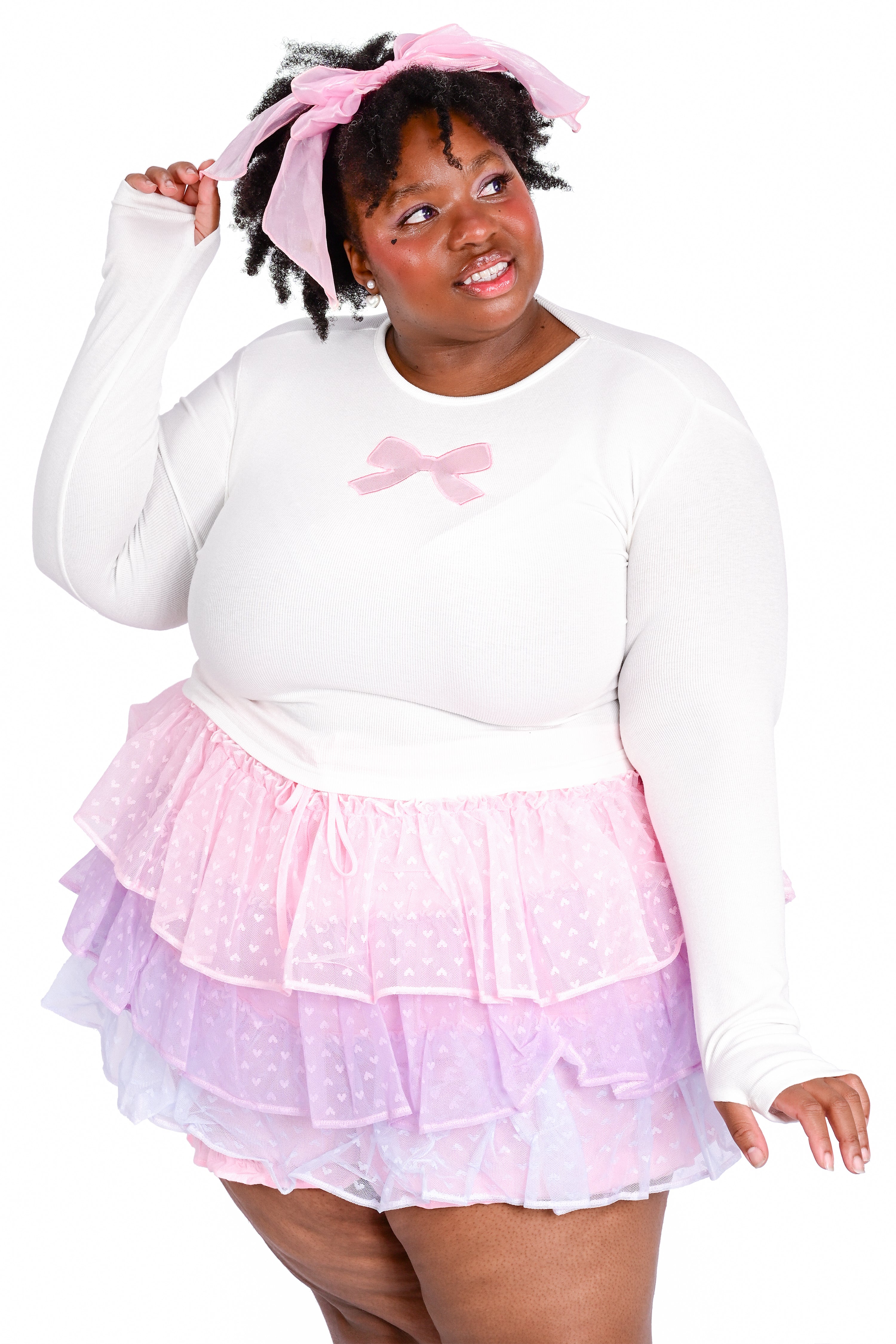 A person wearing a white long sleeve top with a pink ribbon bow cutout detail on the front and a matching ruffled skort