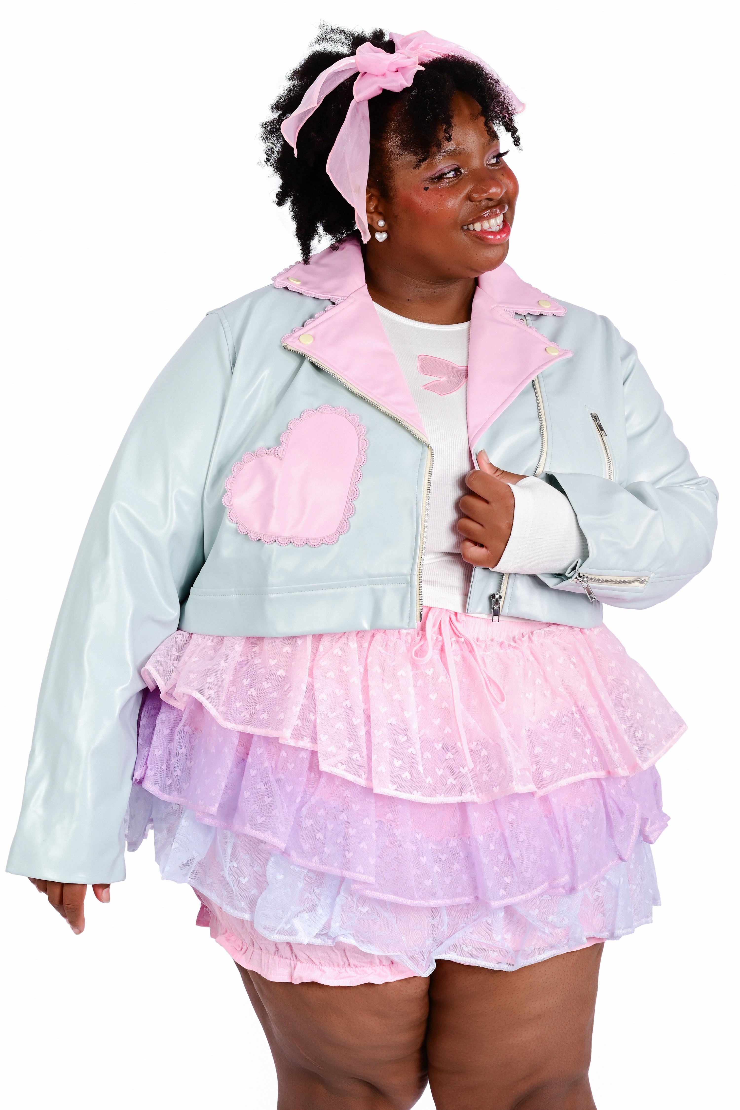 A person wearing a mint green cropped moto jacket with pink accent pockets and lilac trimmed lace, paired with a frilly pink and purple skort.
