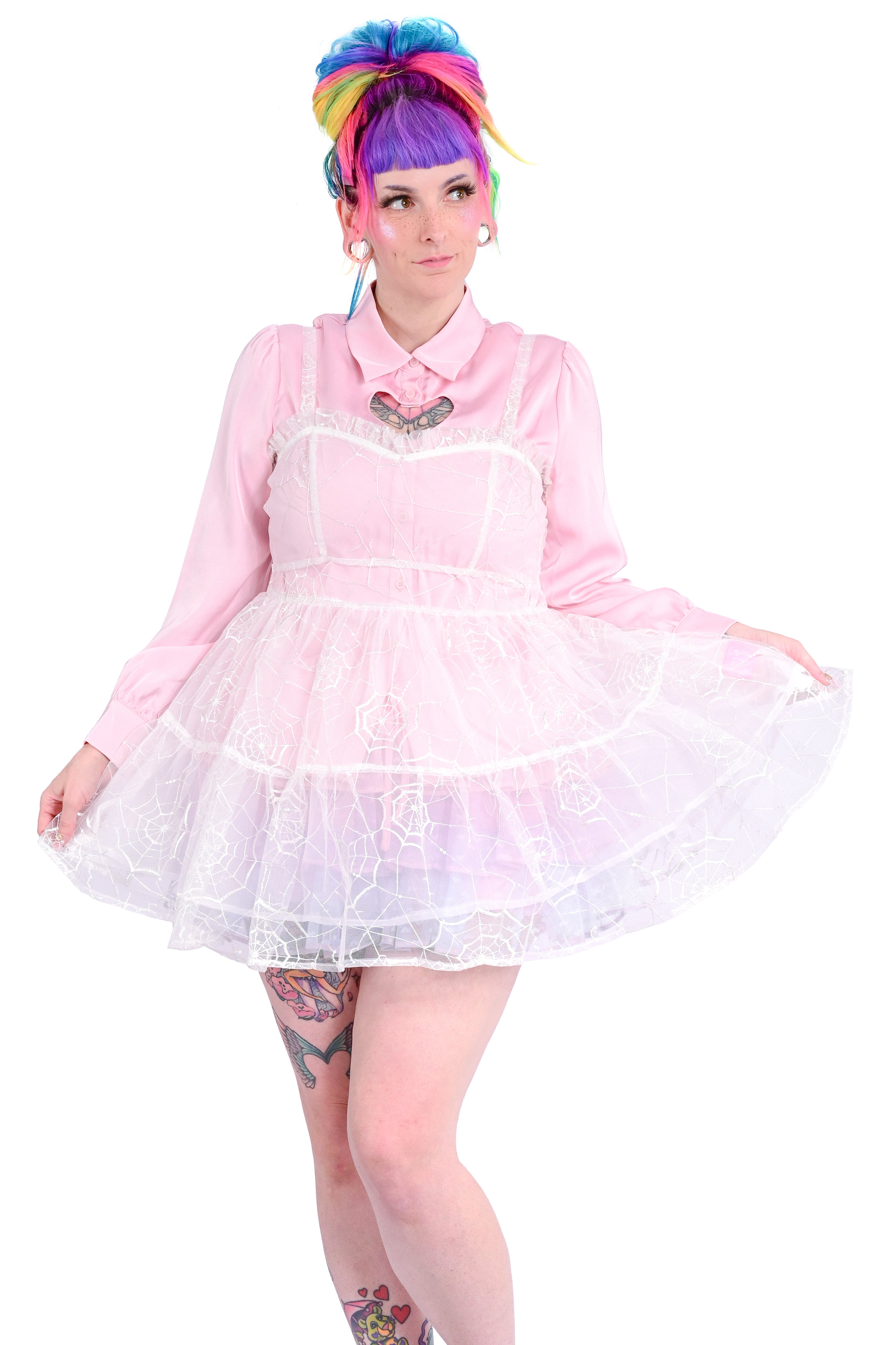 A person wearing a sheer mesh overdress with embroidered cobwebs and sequin dew drops, paired with a pink inner dress.