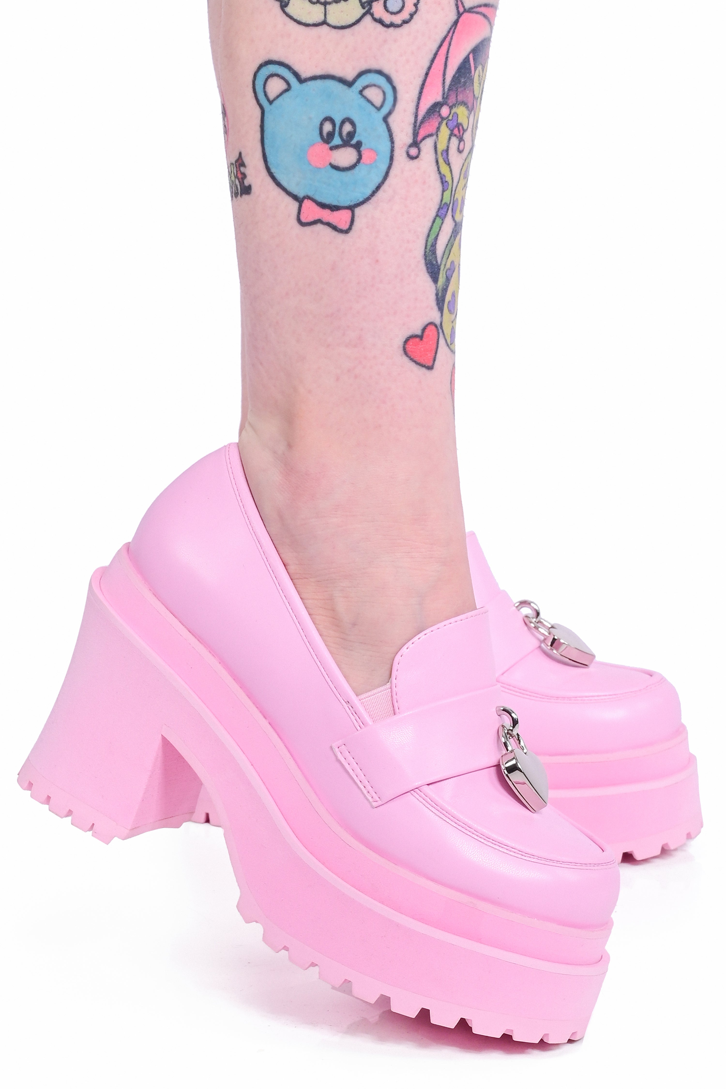 A person wearing a pastel pink platform loafer with a heart padlock detail on the top