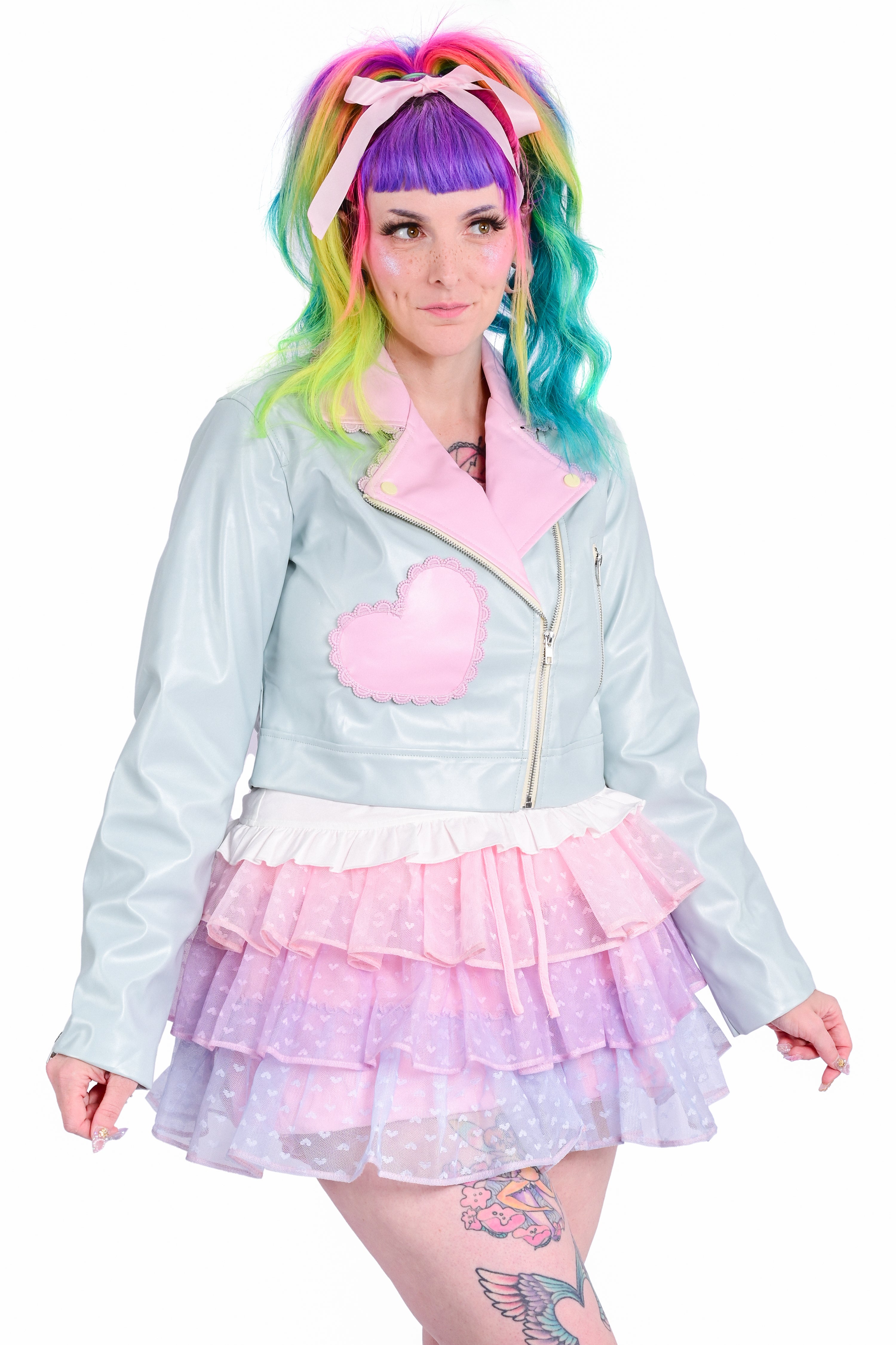 A person wearing a mint green cropped moto jacket with pink accent pockets and lilac trimmed lace, paired with a frilly pink and purple skort.