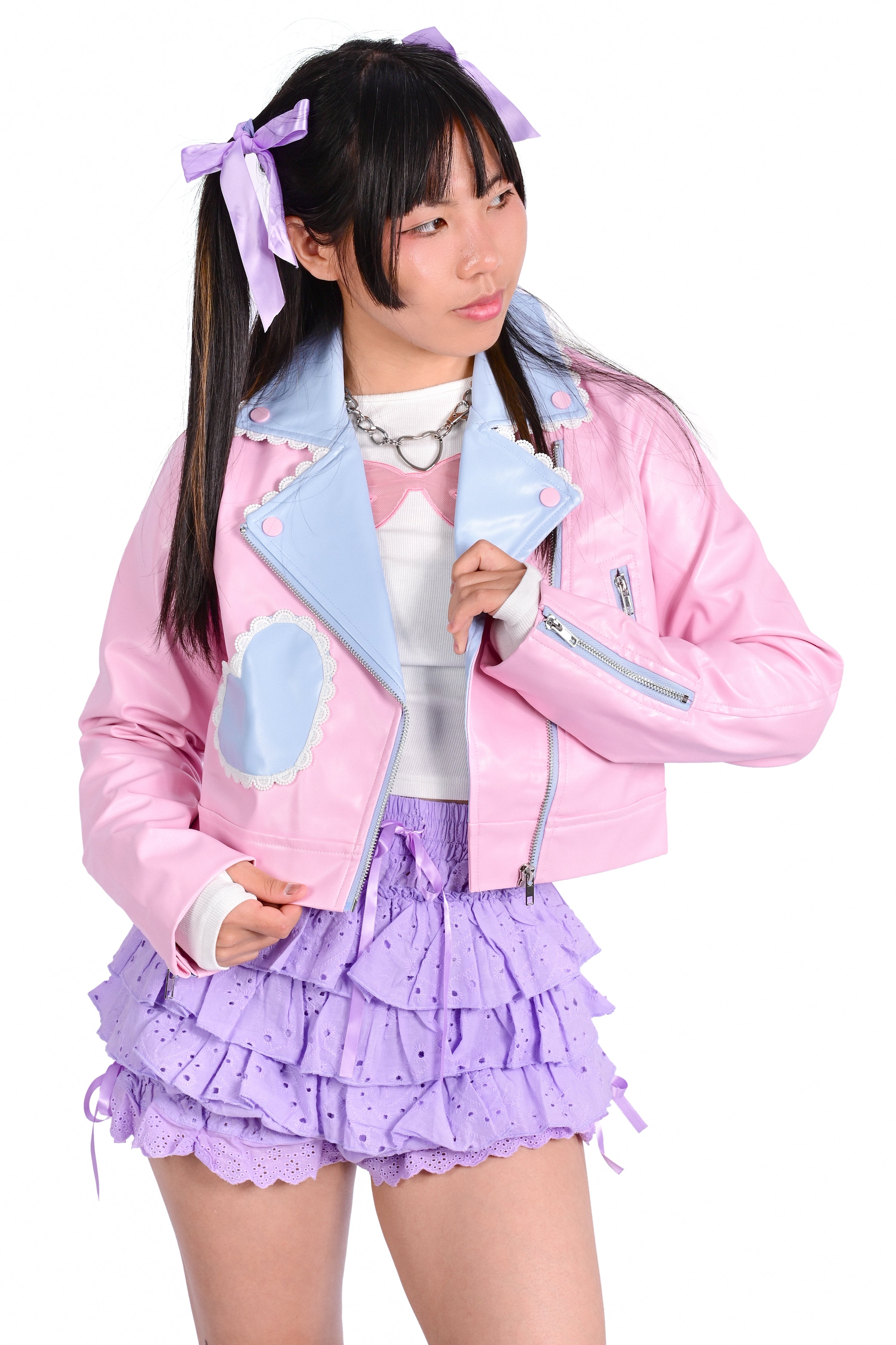 A person wearing a pink cropped moto jacket with blue accent pockets and white trimmed lace, paired with purple ruffled bloomers