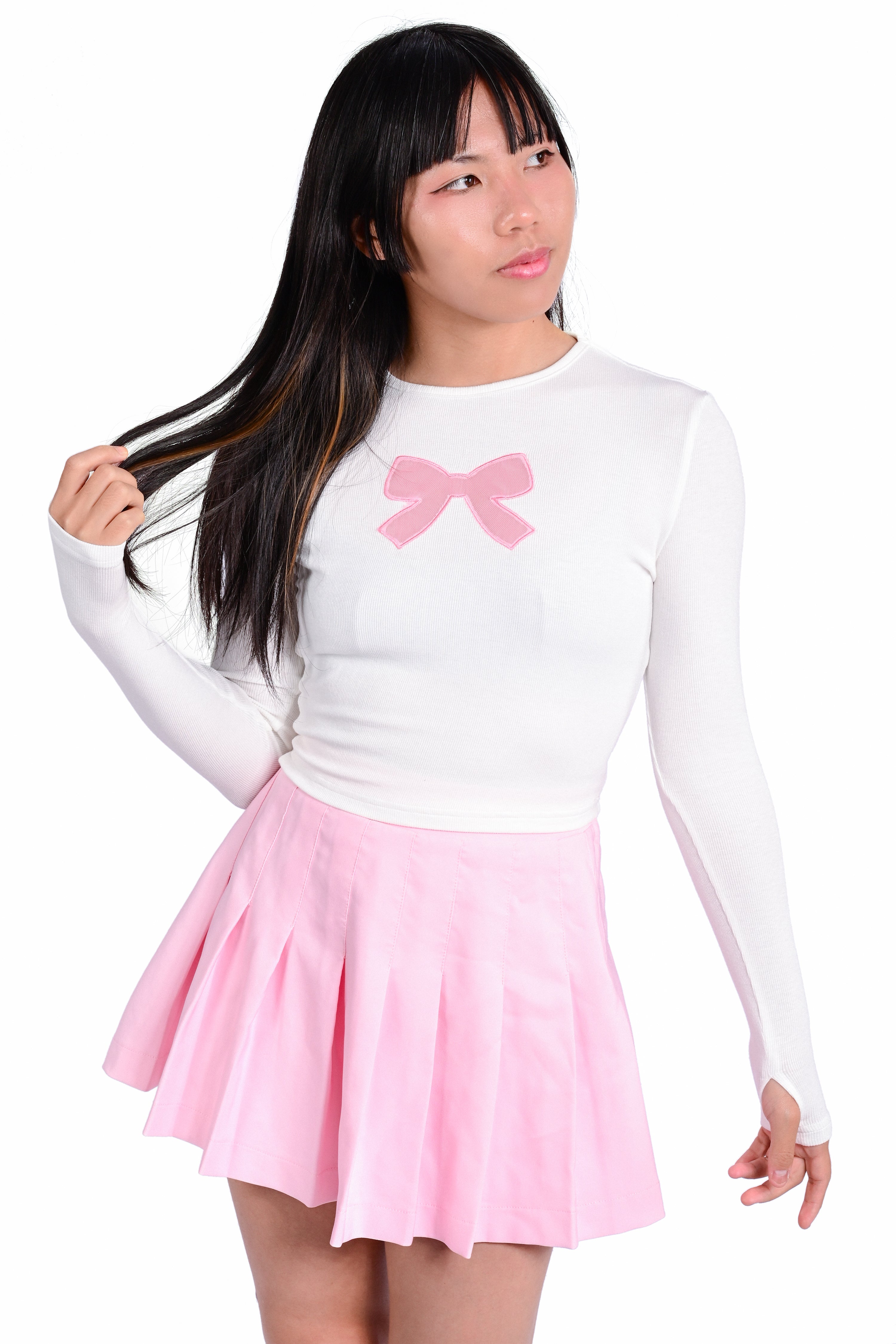 A person wearing a white long sleeve top with a pink ribbon bow cutout detail on the front and a matching pink pleated skirt