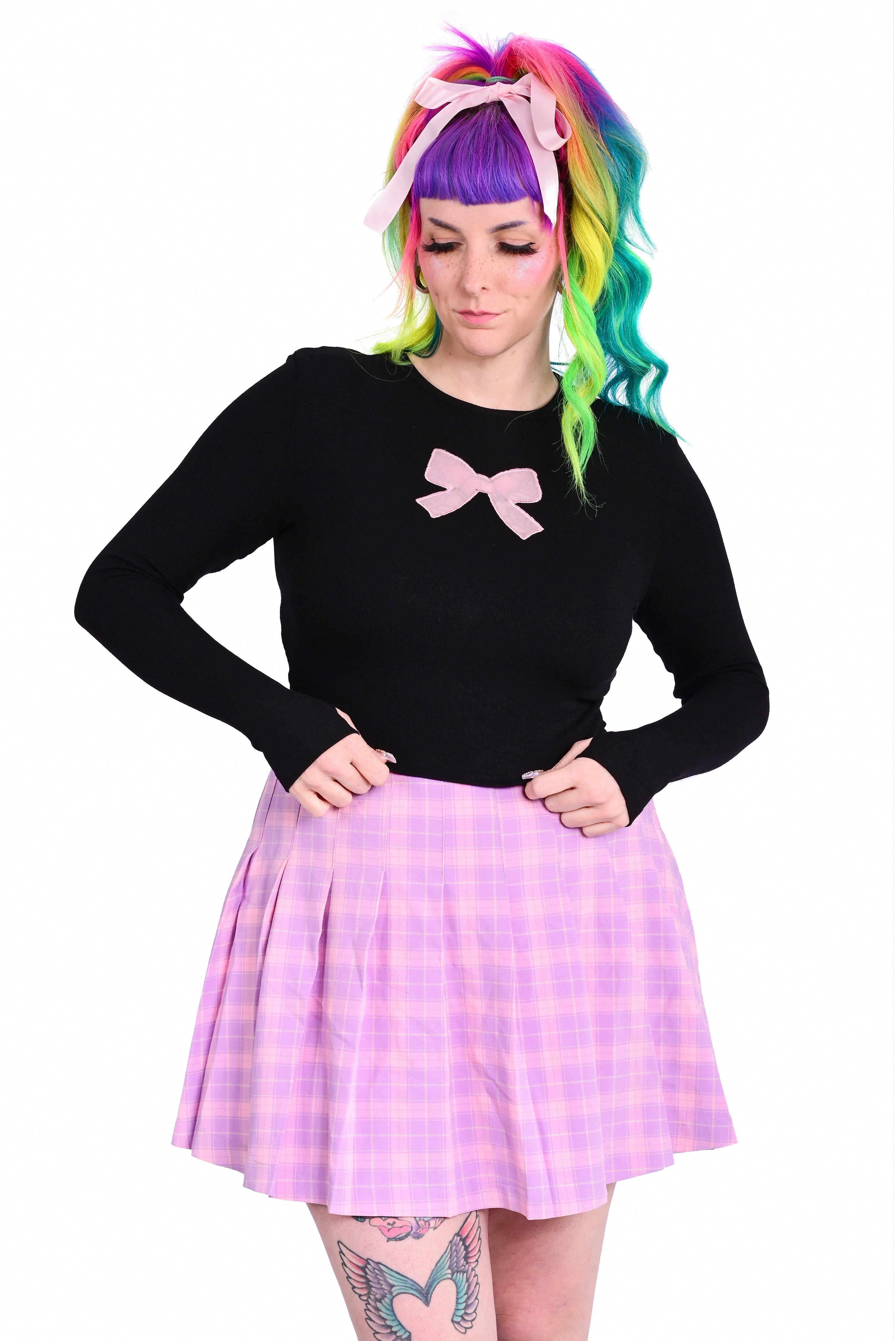 A person wearing a black long sleeve top with a pink ribbon bow cutout on the front and a high-waisted pink checkered skirt.