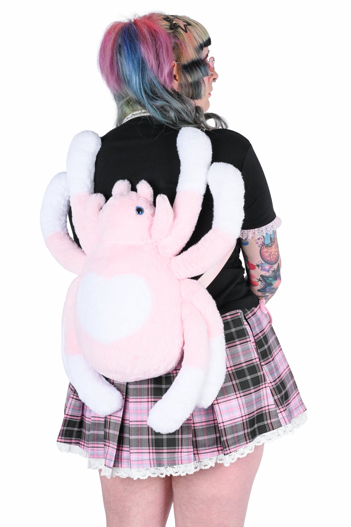 Back view of a model in a pink and black outfit, wearing a large plush spider bag as a backpack.