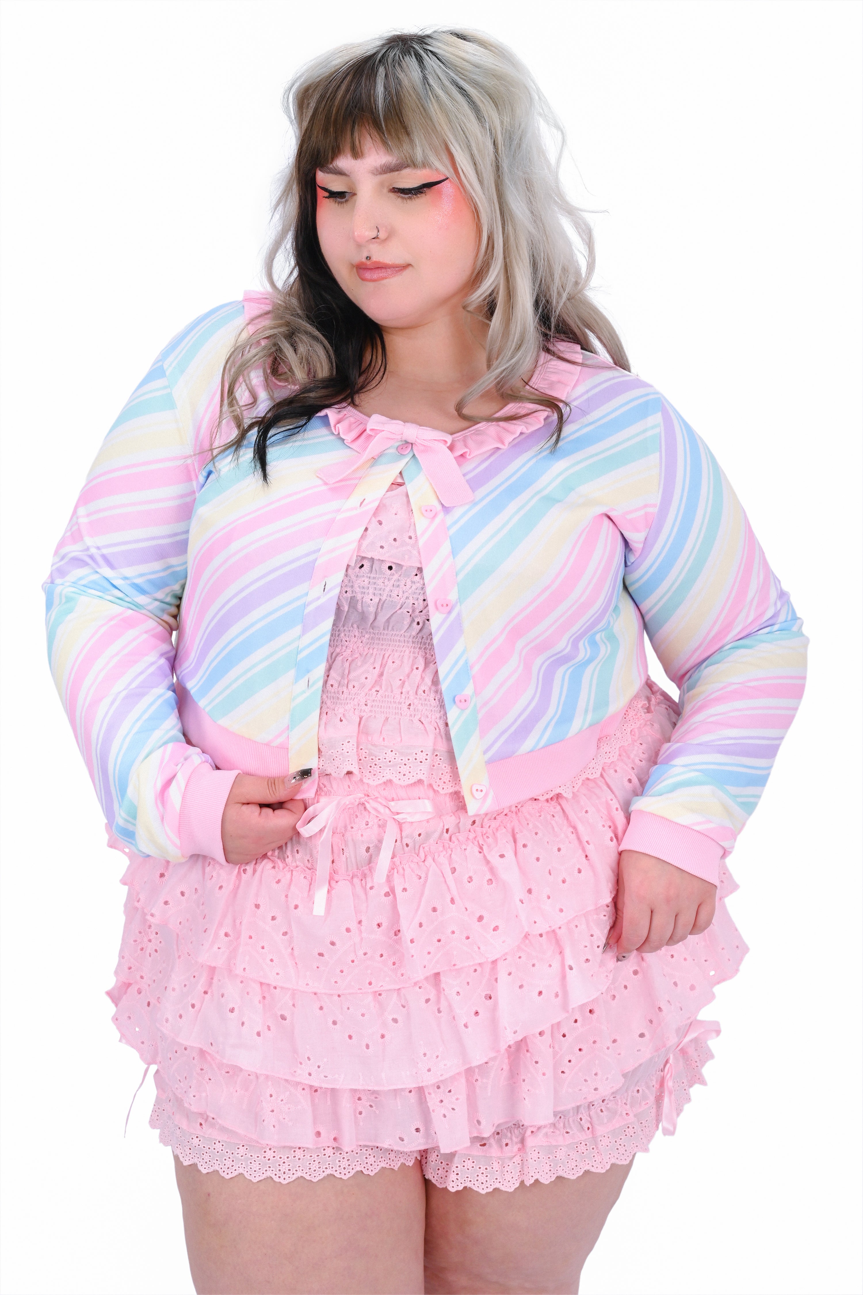 Person wearing a pastel striped cardigan over a pink outfit with ruffles on a white background