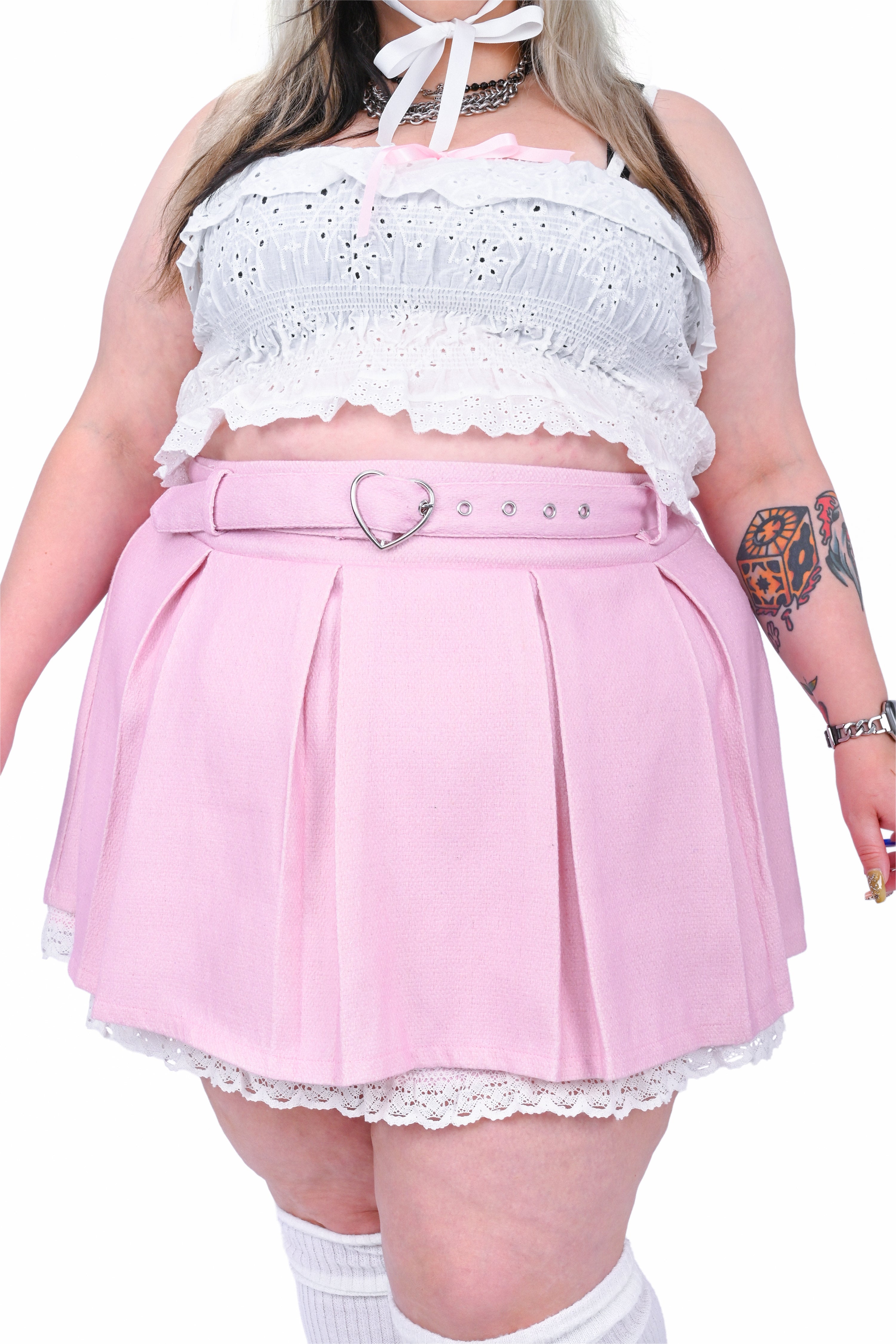 Person wearing a white lace top and pink pleated skirt with a heart-shaped belt.