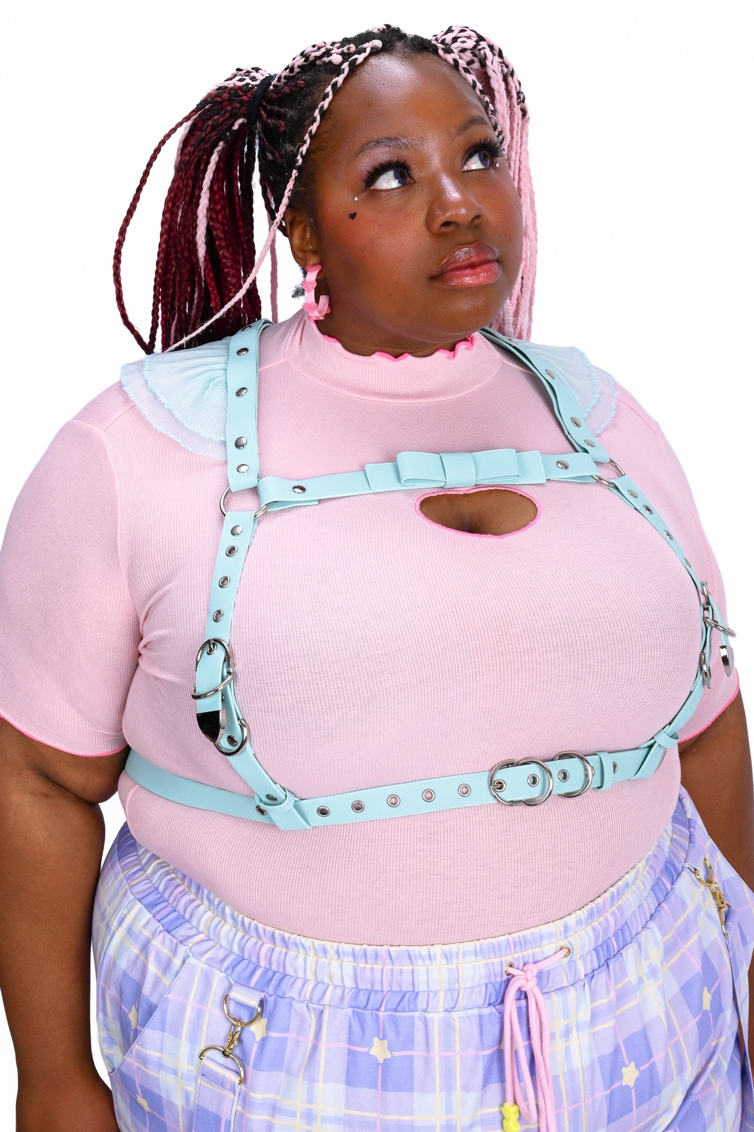 Person wearing a pink top with cut-out design and plaid pants on a white background