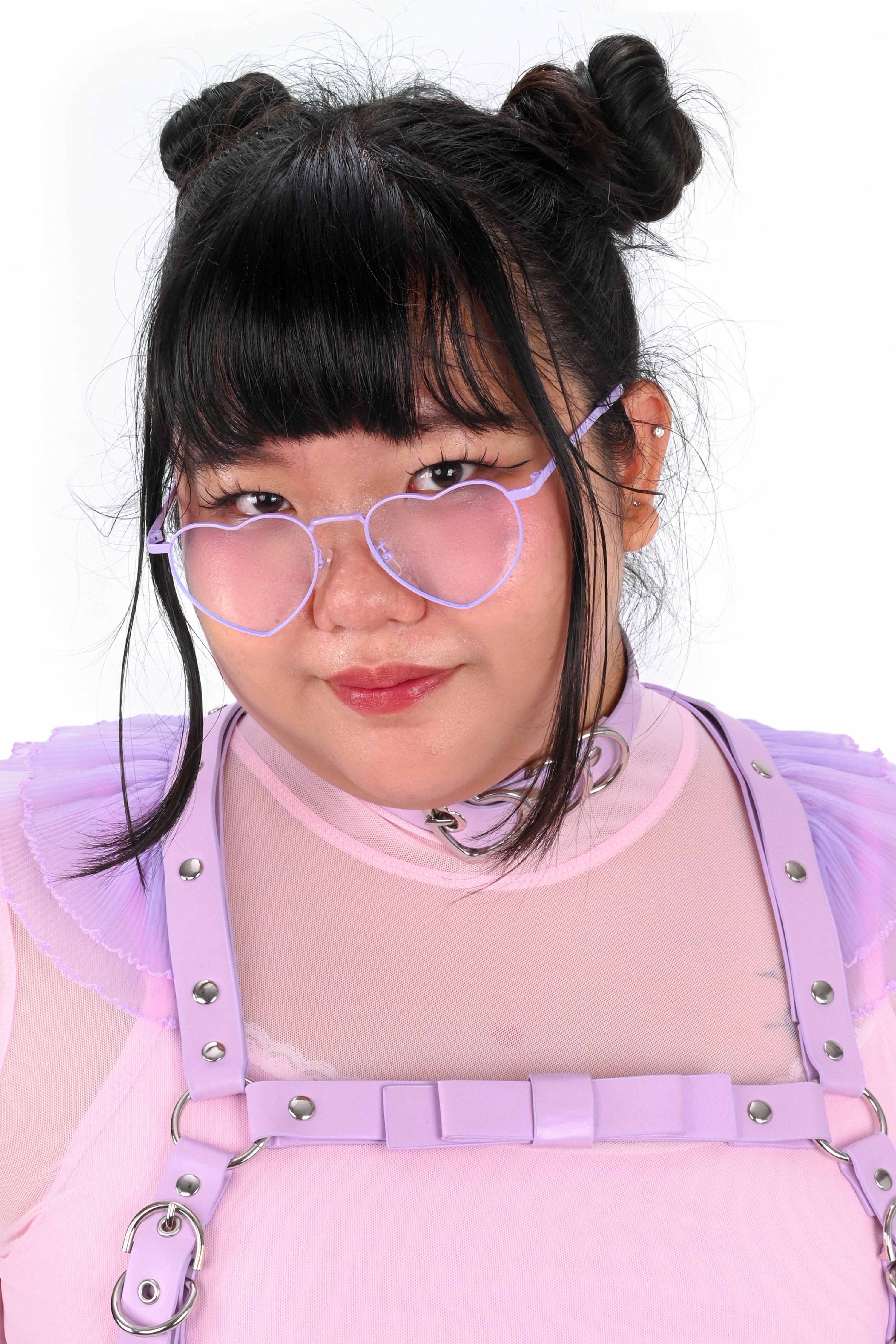 Person wearing pink heart-shaped glasses and a pink outfit with suspenders on a white background
