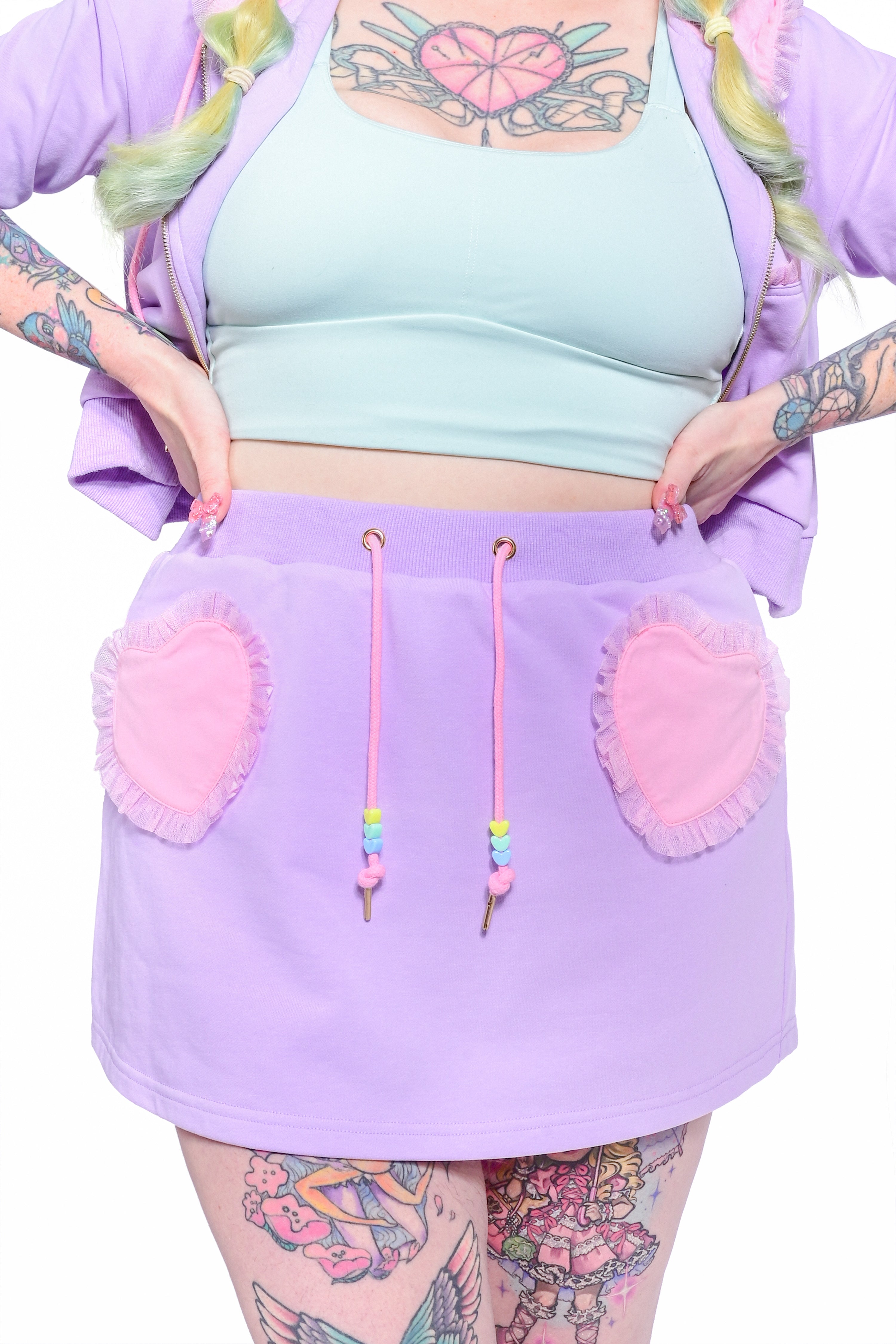 A person wearing a purple skort with heart-shaped pockets and a braided drawstring with pink heart bead detailing.