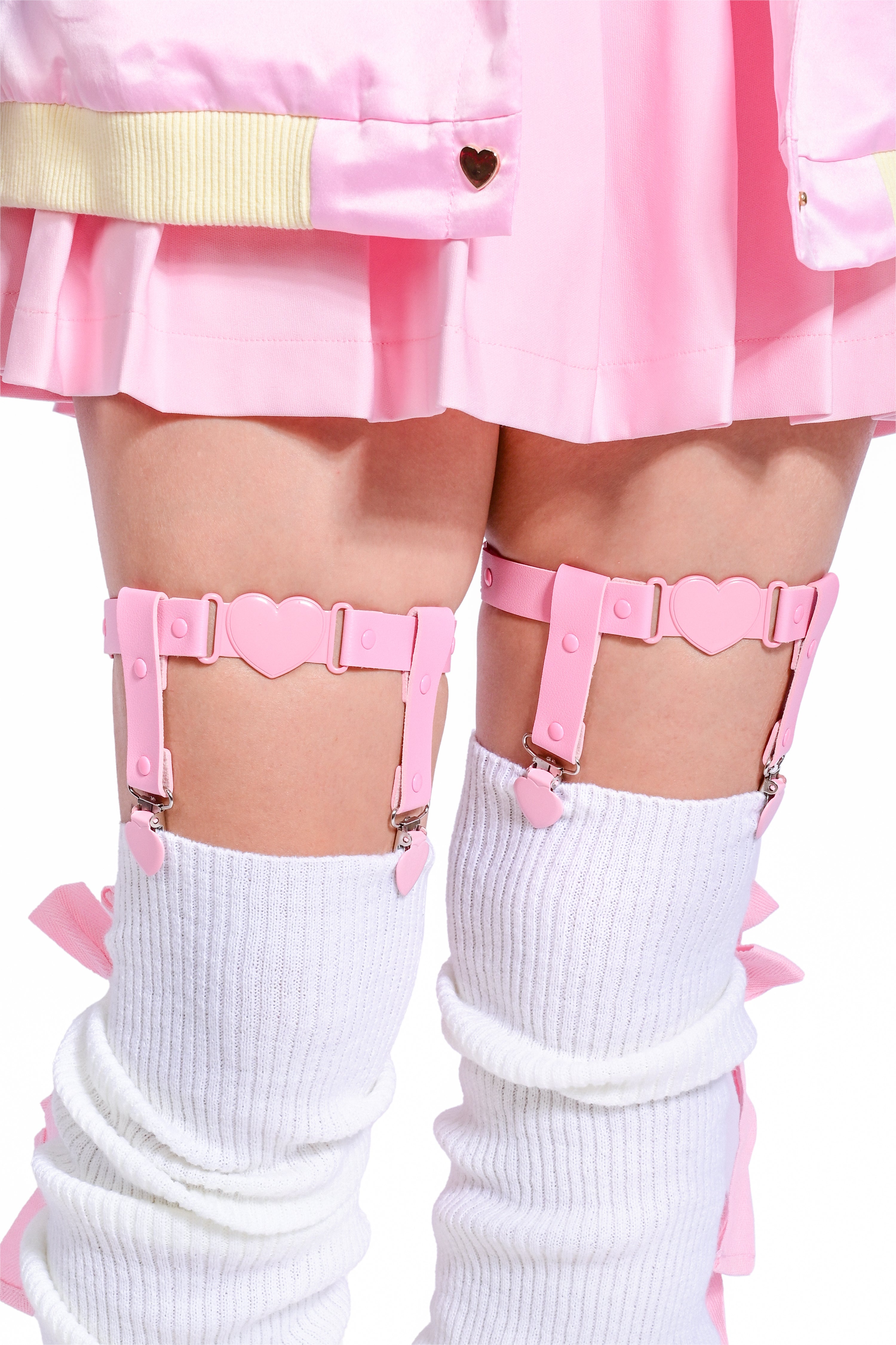 A set of pink leg garters with vegan leather detailing and metal hardware, paired with white thigh-high legwarmers.