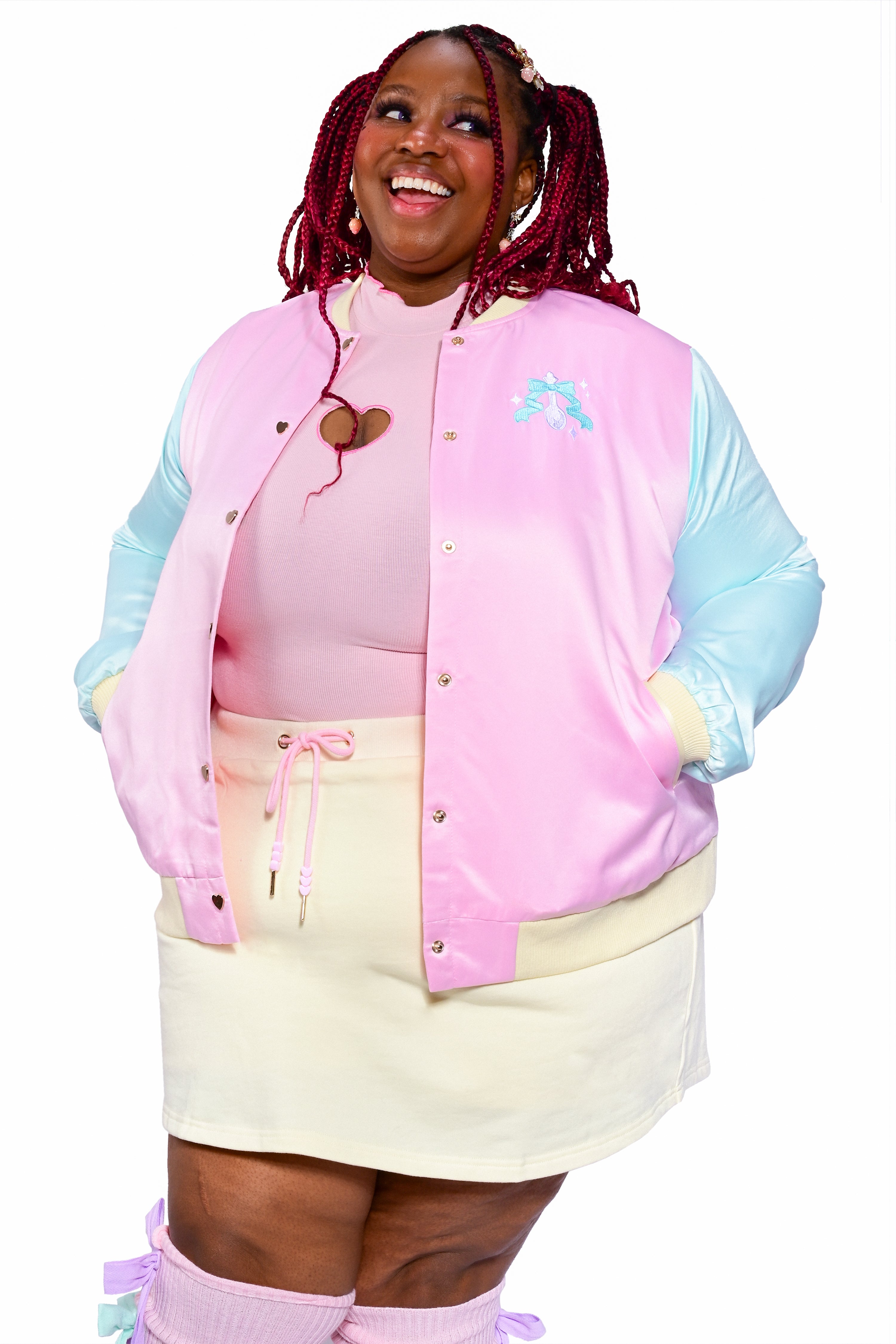 A person wearing an embroidered satin color blocked varsity jacket in pink, blue, and yellow.