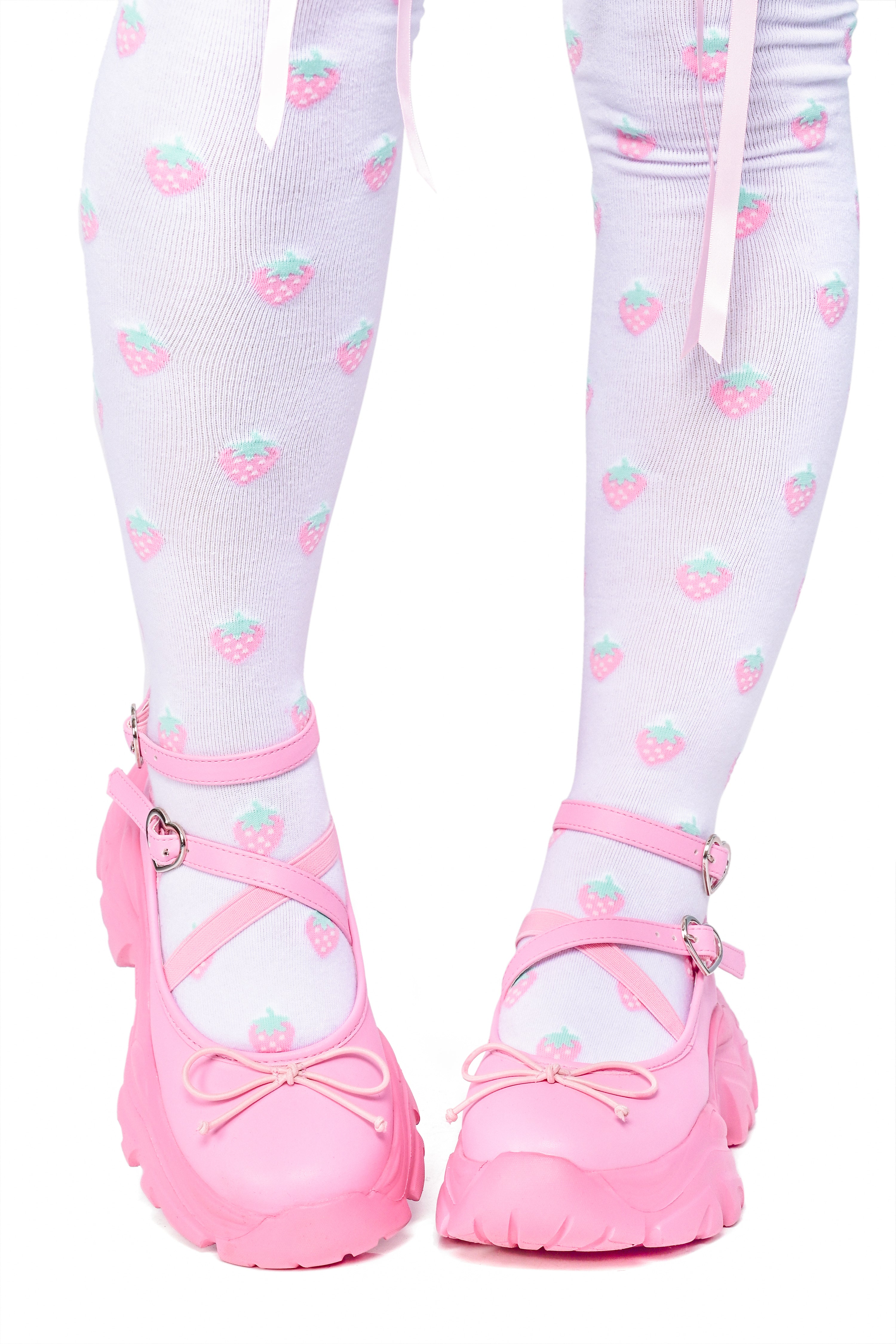 Person wearing pink ballet sneakers with heart buckle straps and a platform sole.