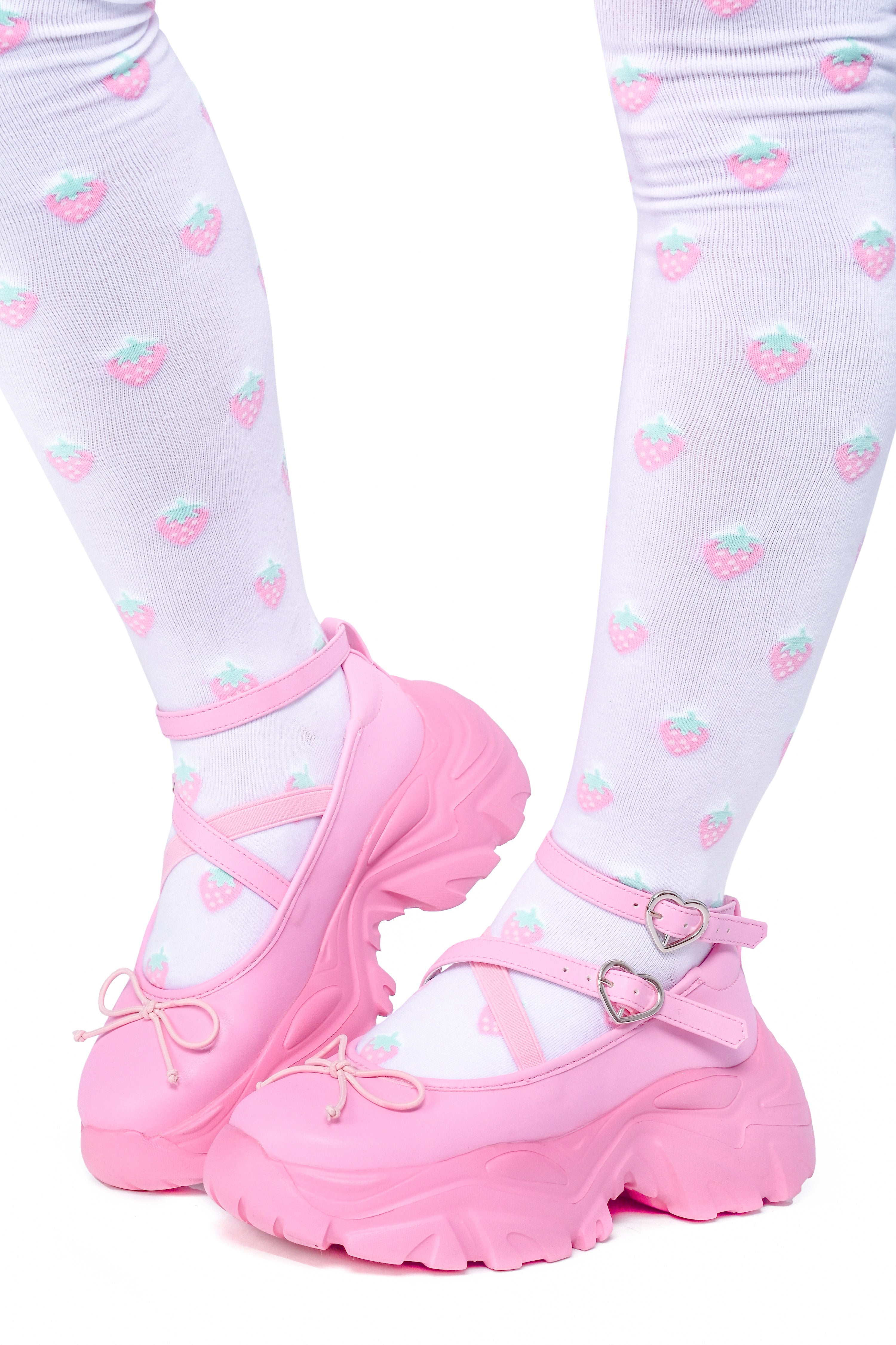 Person wearing pink ballet sneakers with heart buckle straps and a platform sole.