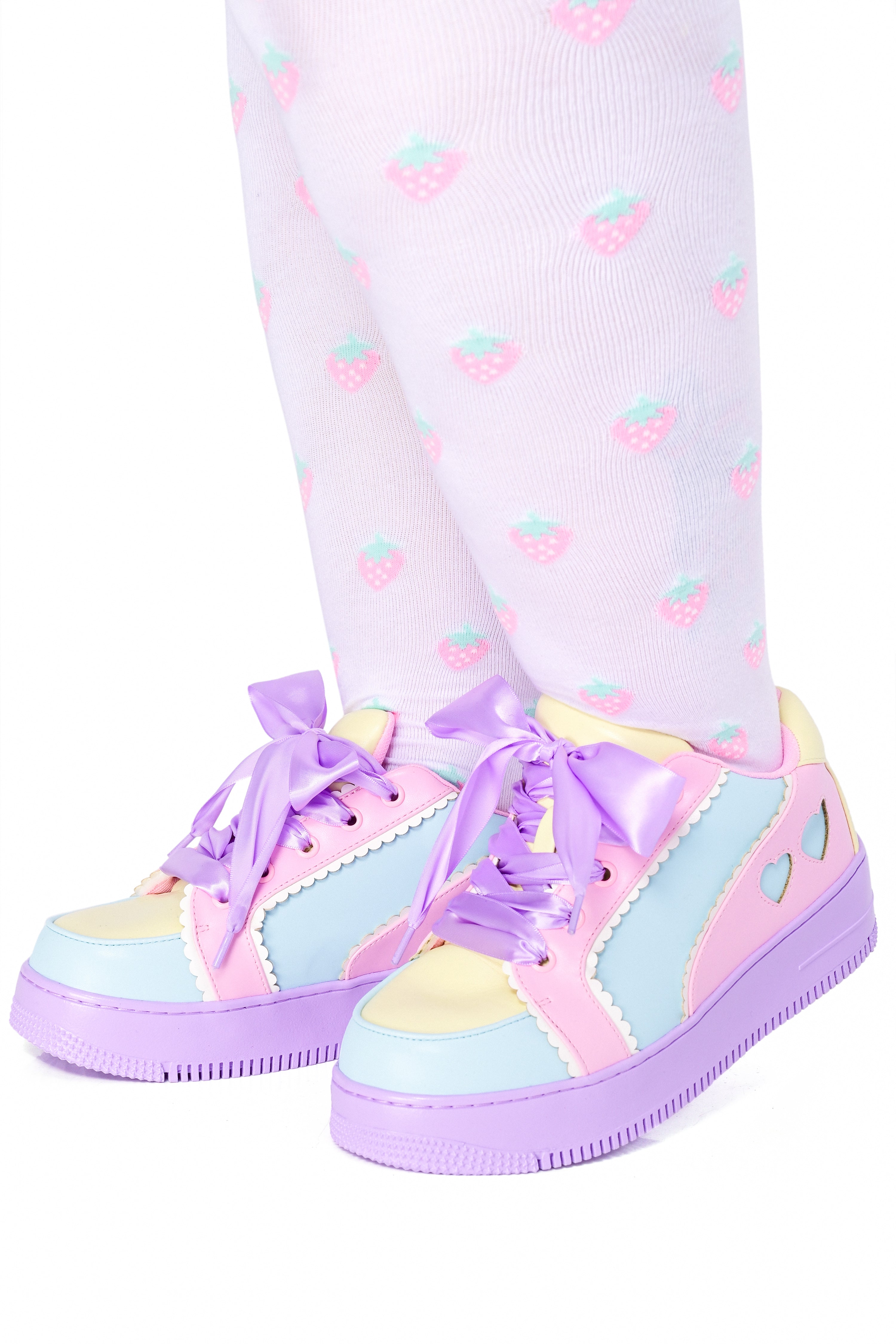 A person wearing pastel colorblock sneakers with heart accents and scalloped trim details. The sneakers are pink, purple, and yellow, paired with matching socks.