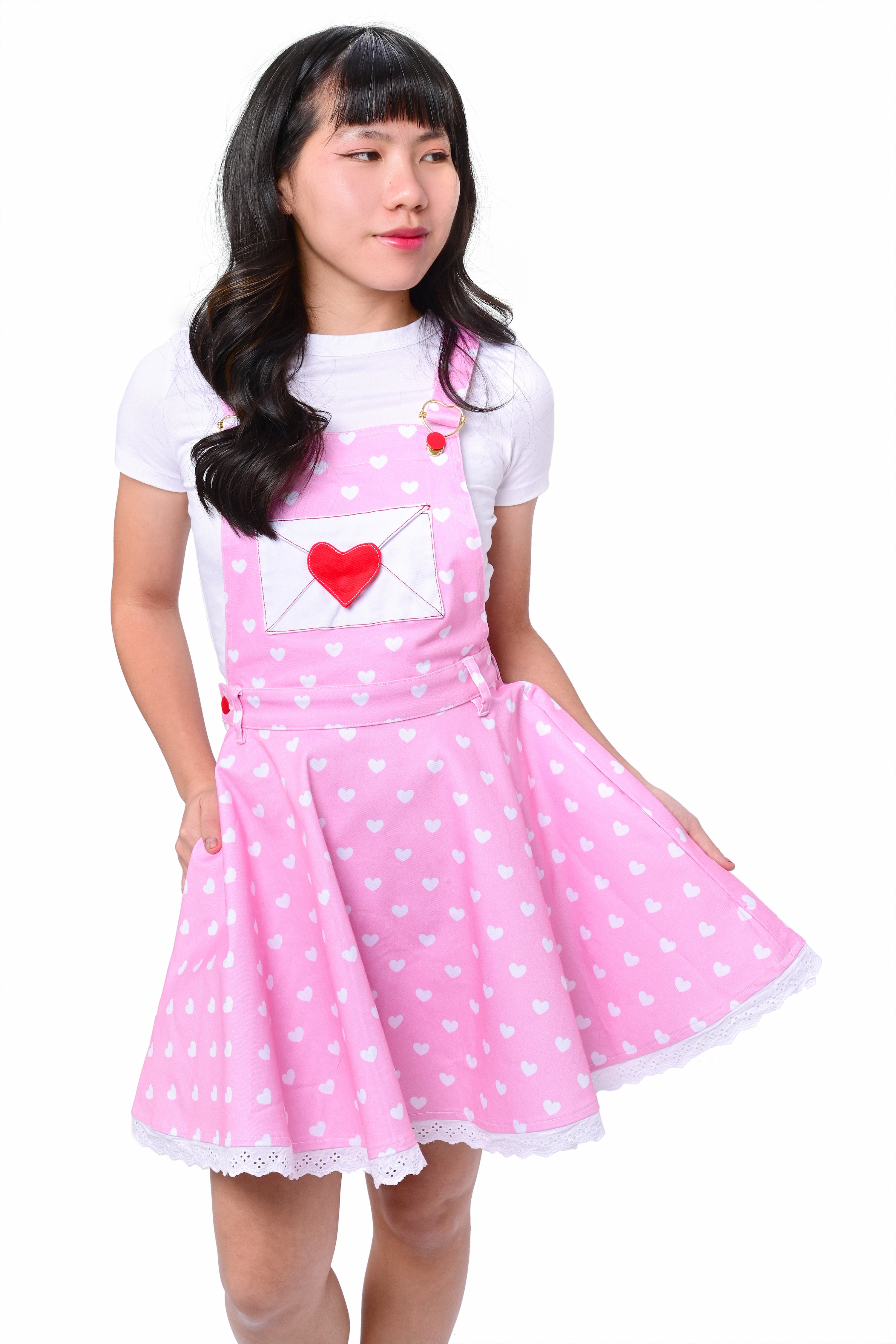A person wearing a pink heart-printed pinafore dress with red buttons and heart-shaped hardware on the straps.
