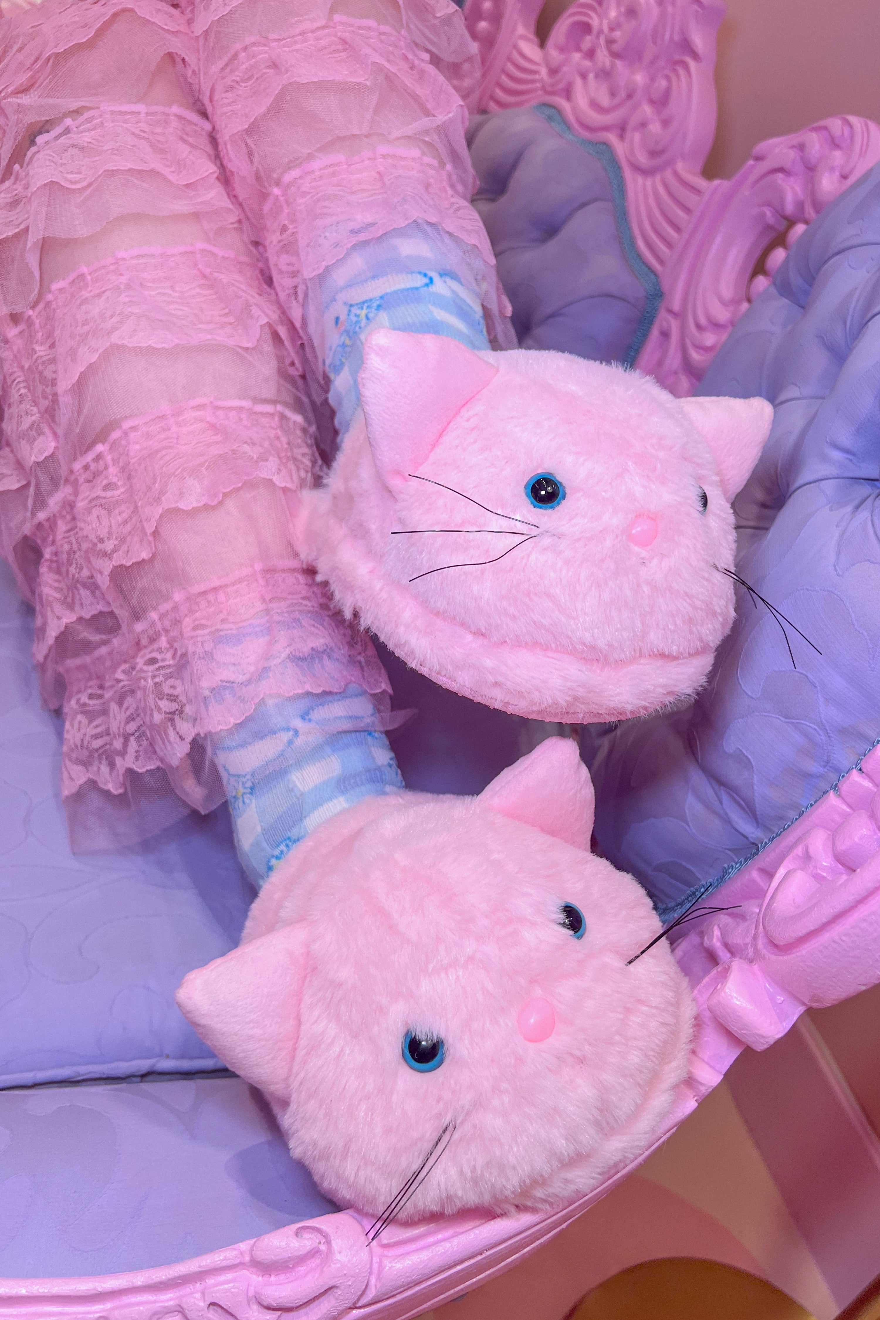 A model wearing a pair of pink fluffy slippers designed to look like cats
