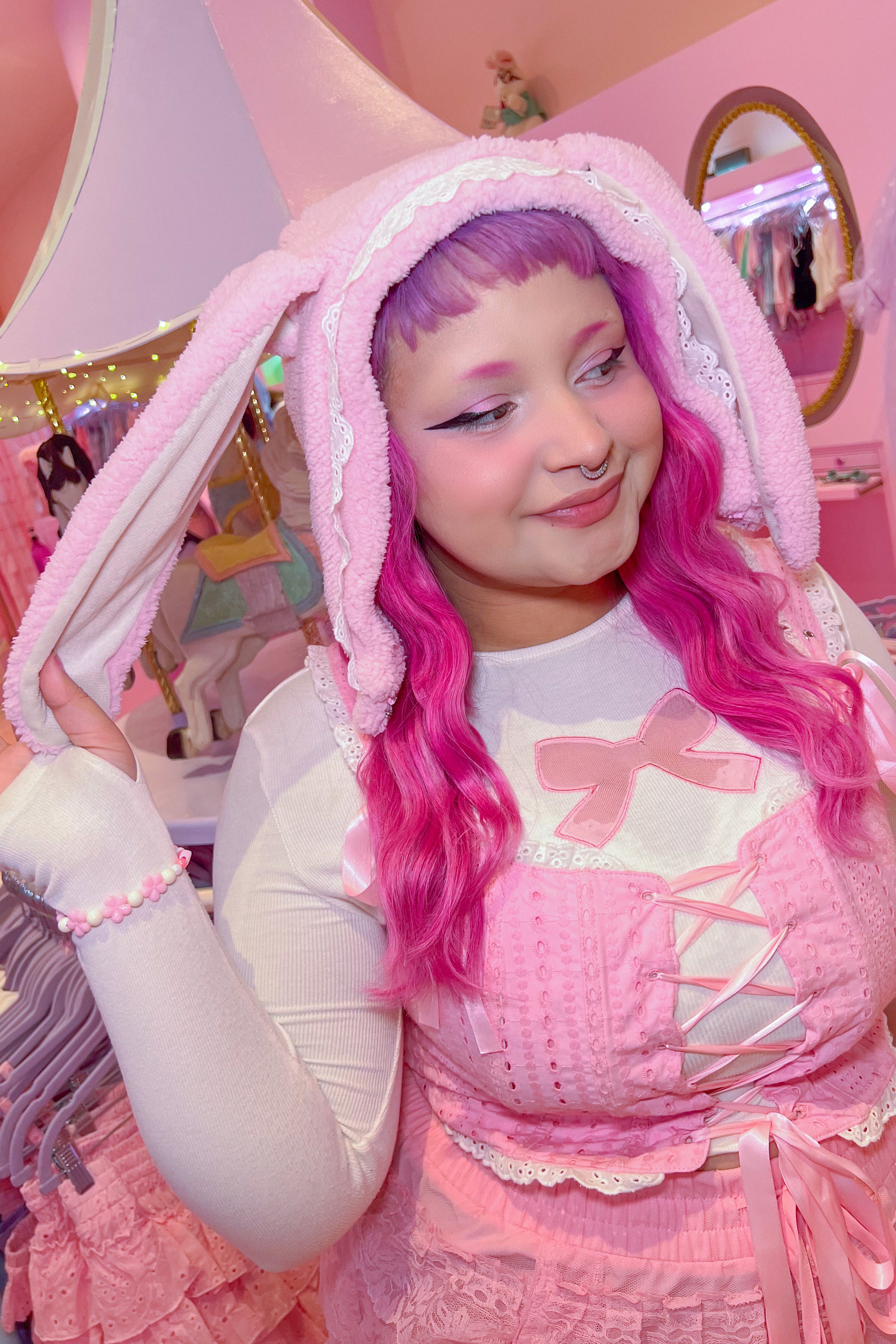 A person wearing a pink bunny hooded scarf with detachable extensions, paired with a white top and a pink pants.