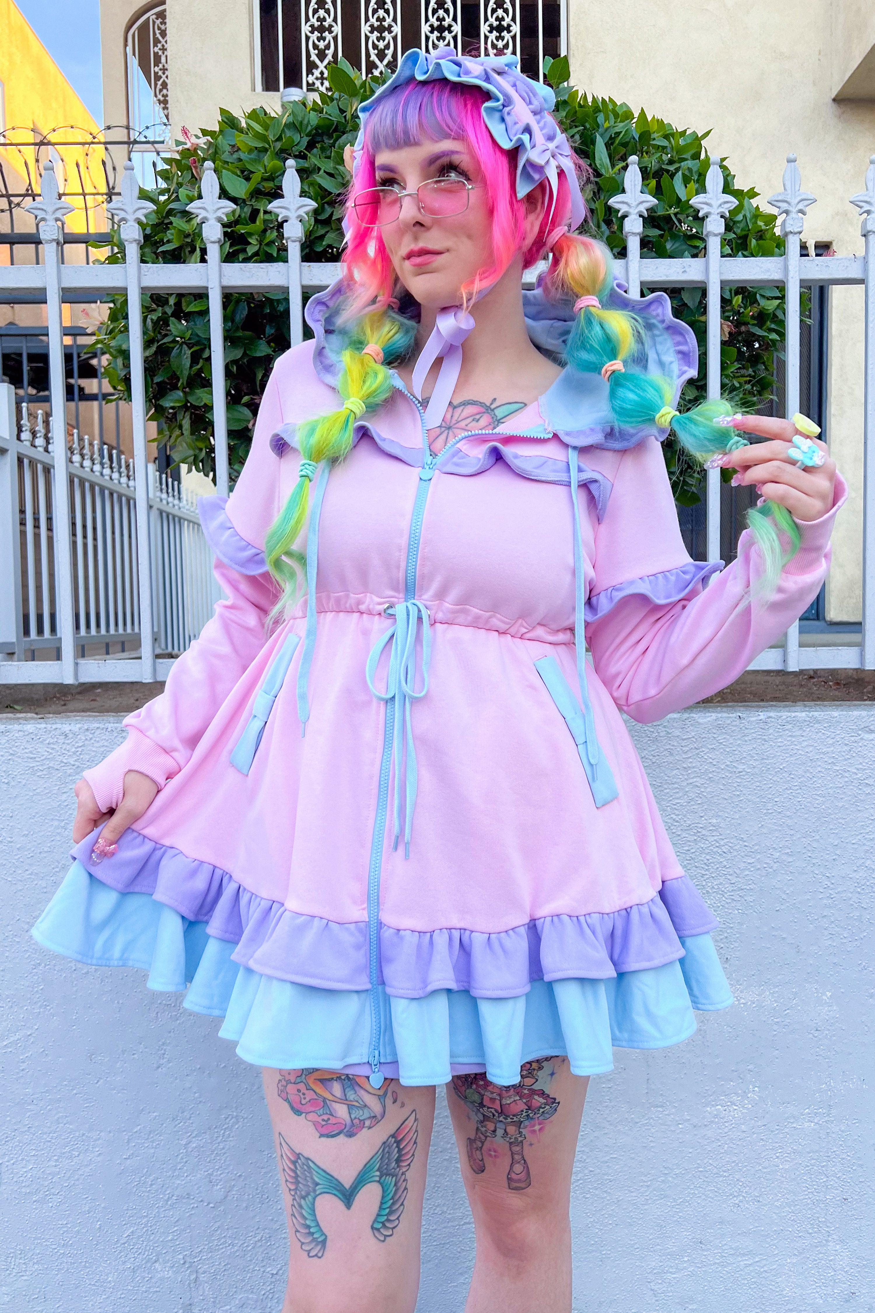 A person wearing a pink hoodie dress set with long sleeves, hood, and ruffled skirt, paired with a matching headdress