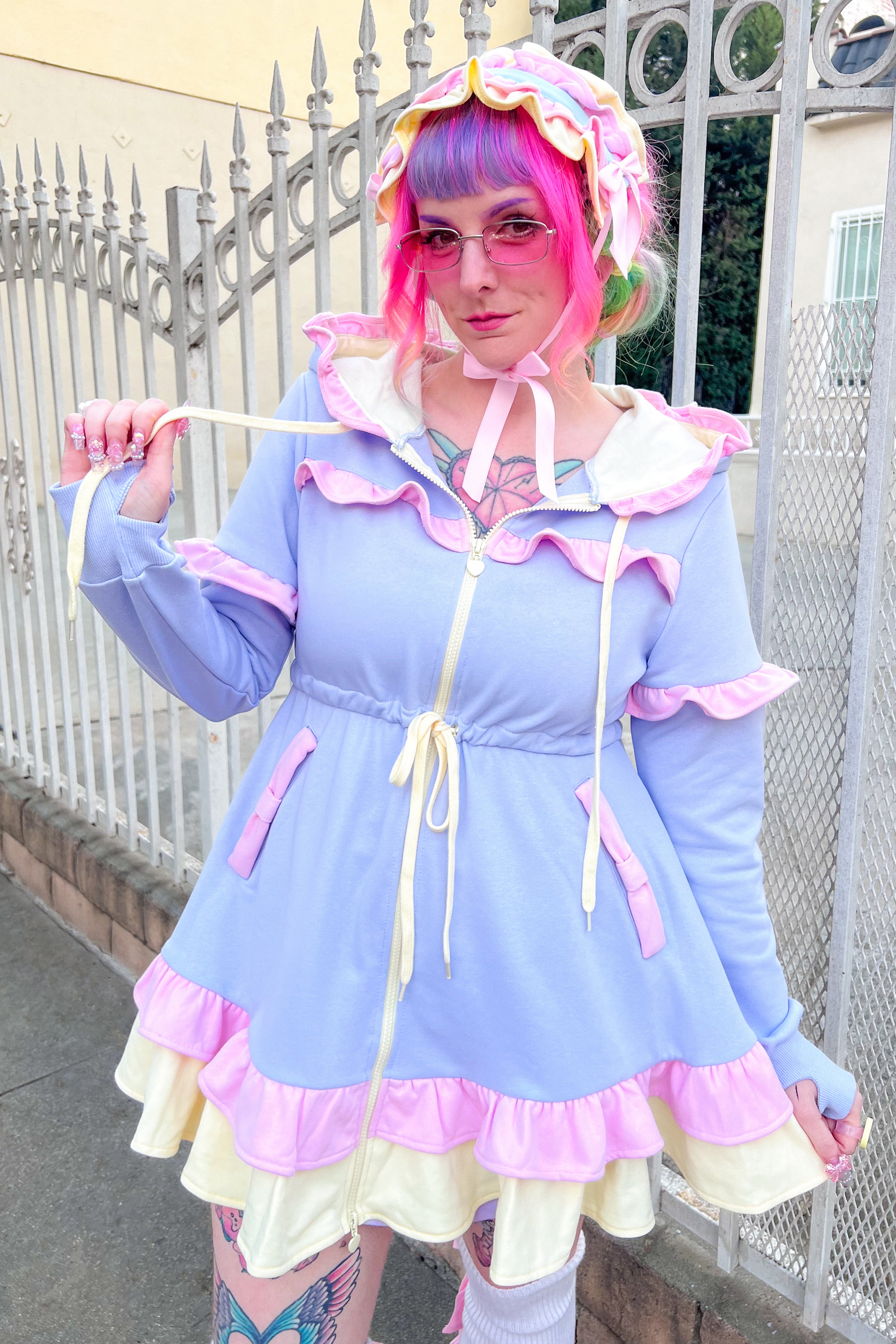 A person wearing a periwinkle hoodie dress set with long sleeves, hood, and ruffled skirt, paired with a matching headdress
