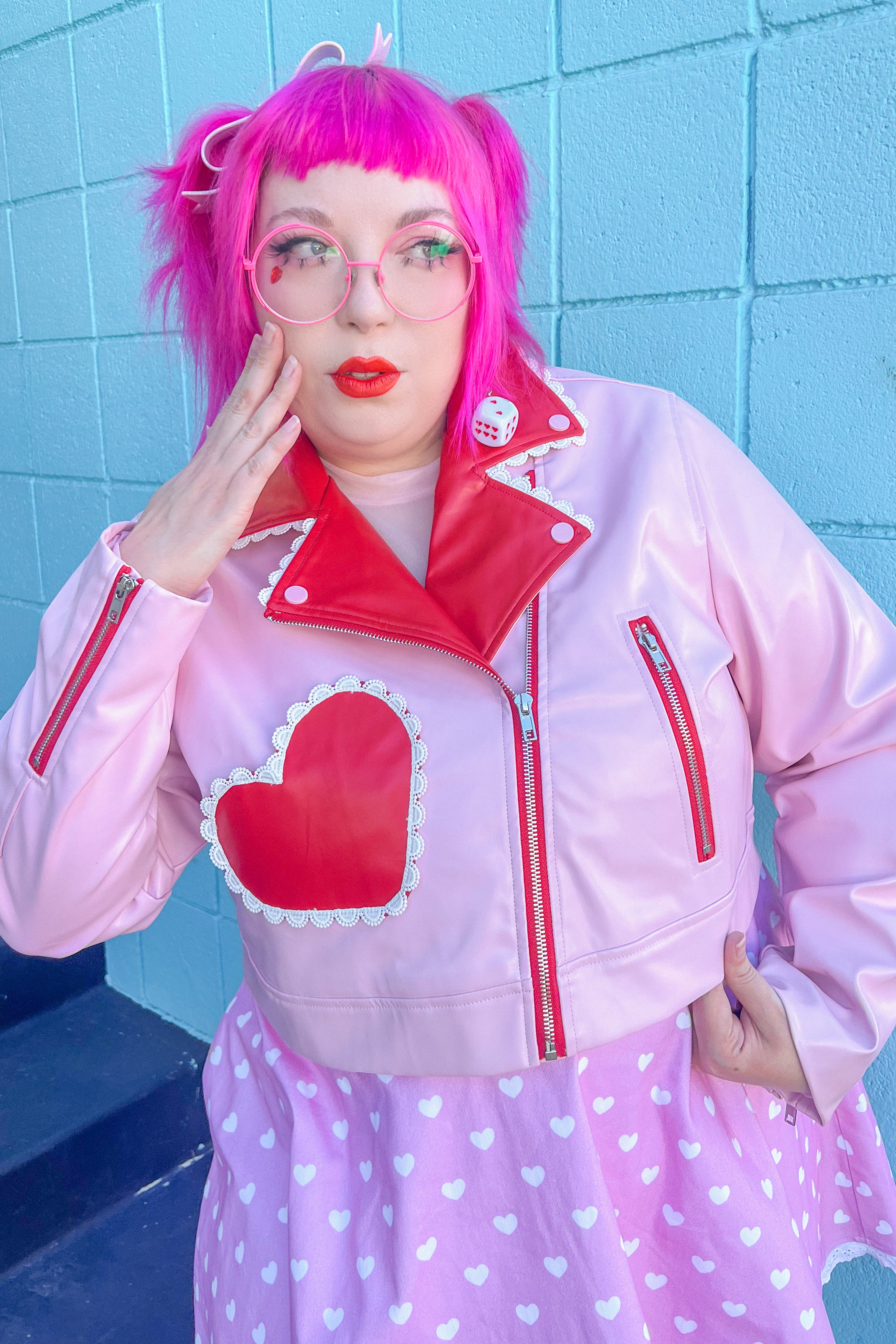 A person wearing a red and pink cropped moto jacket with heart accents, paired with a pink dress.