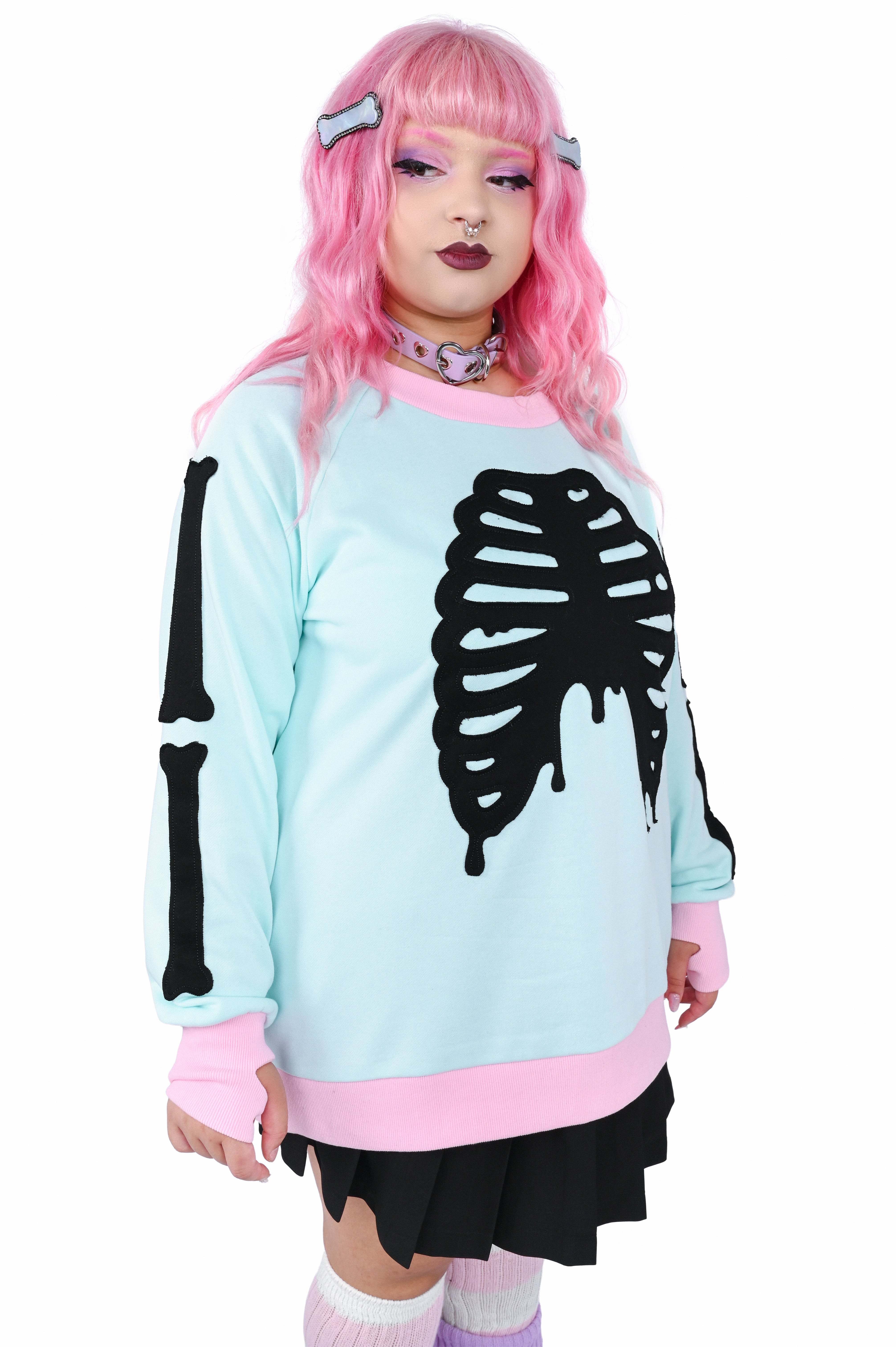Model wearing a mint colored pullover sweater with pink trim and black skeleton appliqué